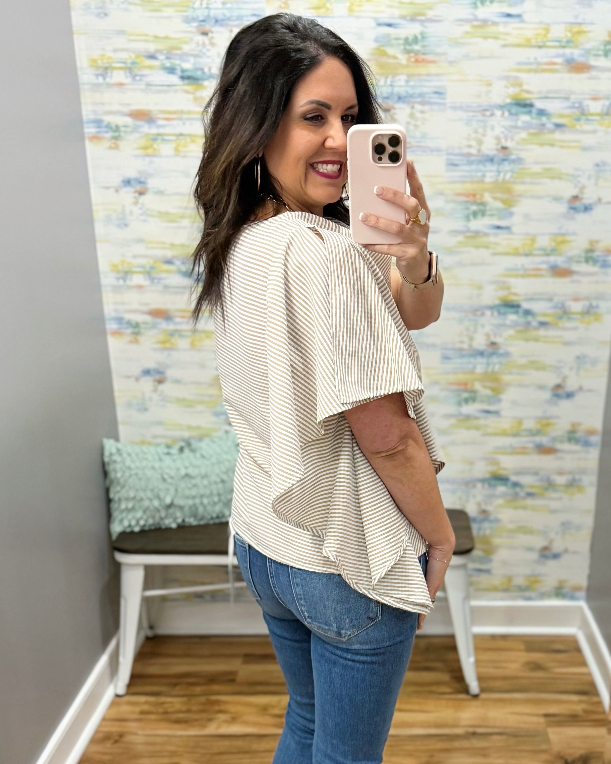 Woman taking a mirror selfie wearing a striped top and jeans in a room with a textured wall.