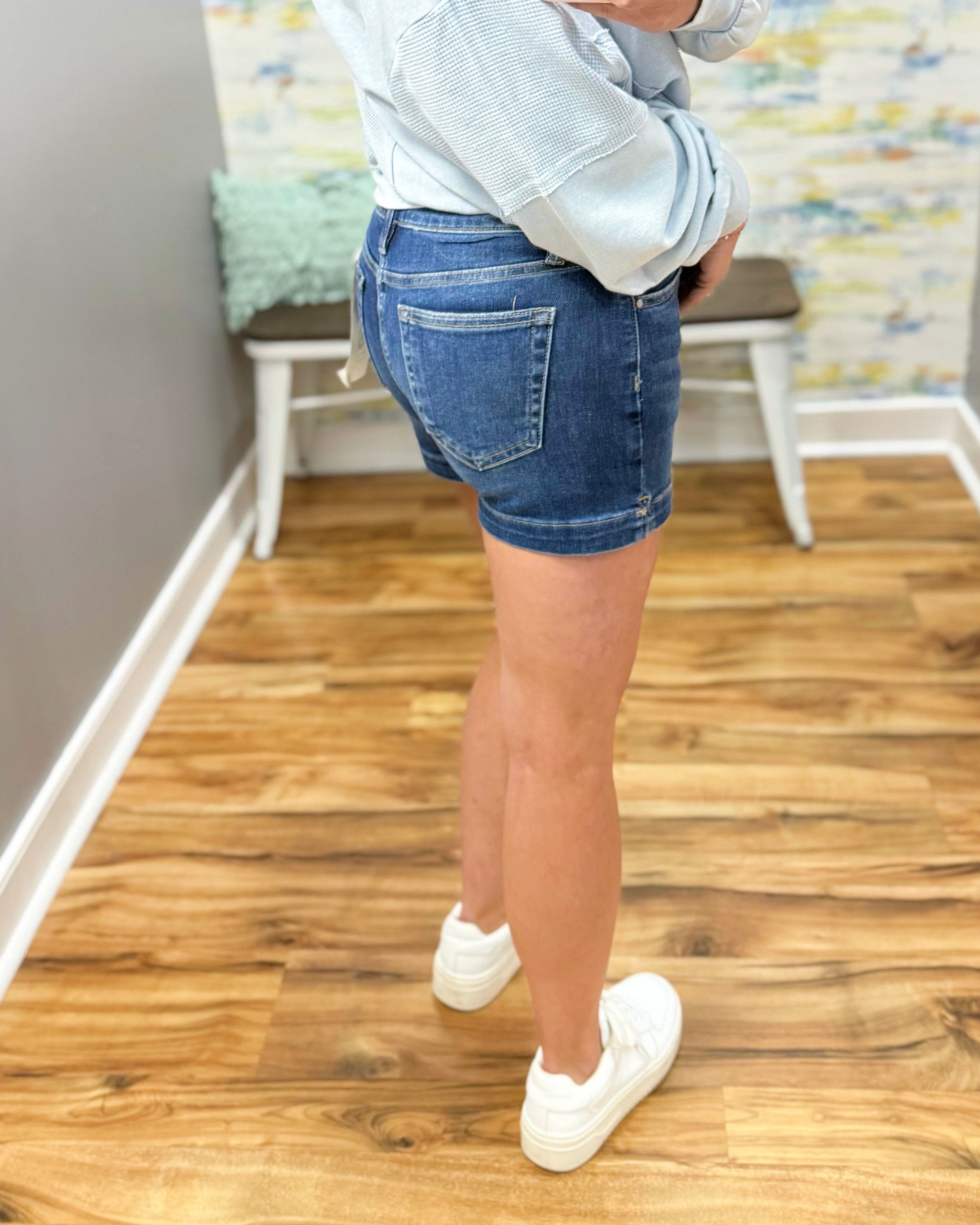 Person wearing blue denim shorts and white sneakers on a wooden floor.