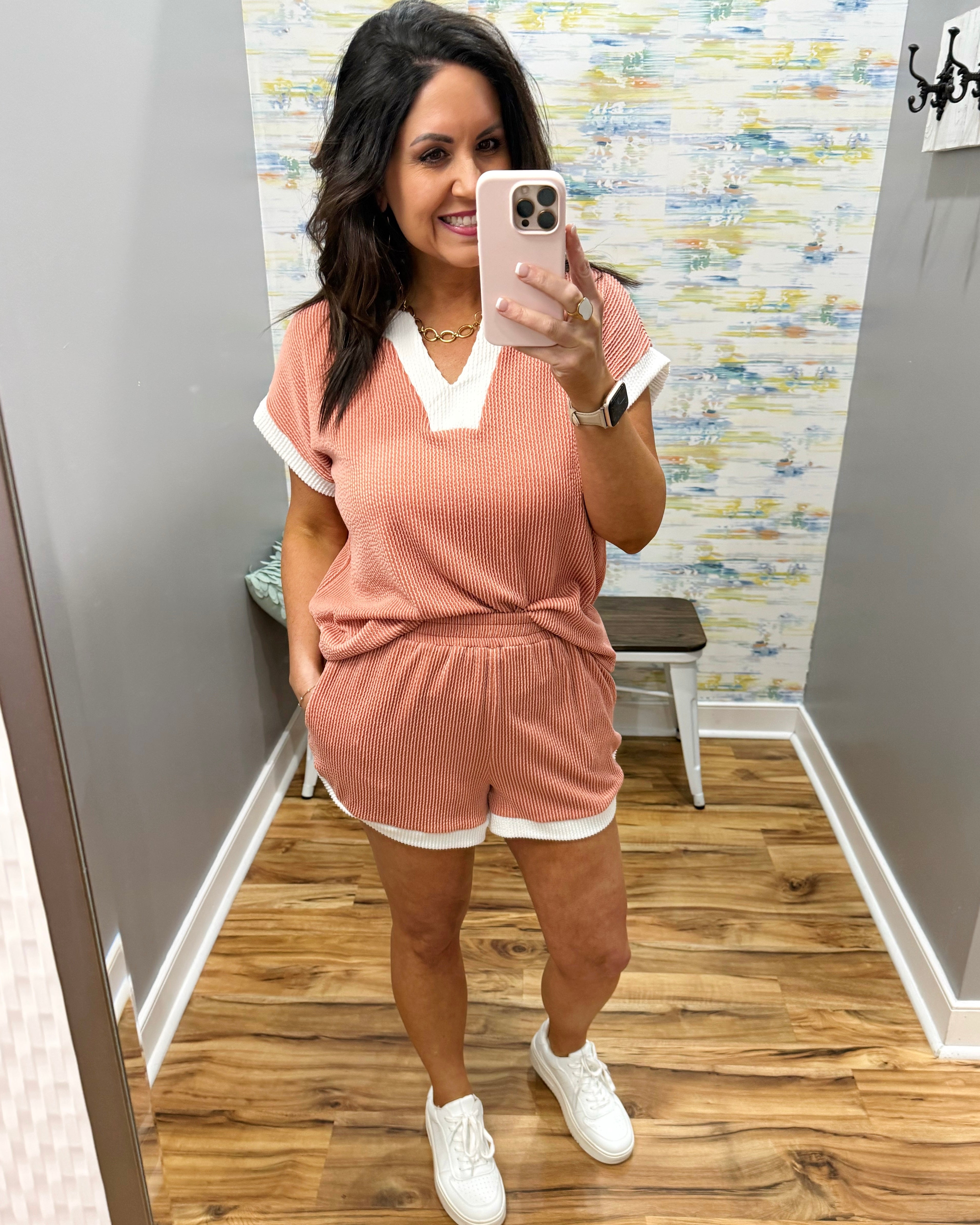 Woman taking a mirror selfie wearing a pink ribbed lounge set with white accents.