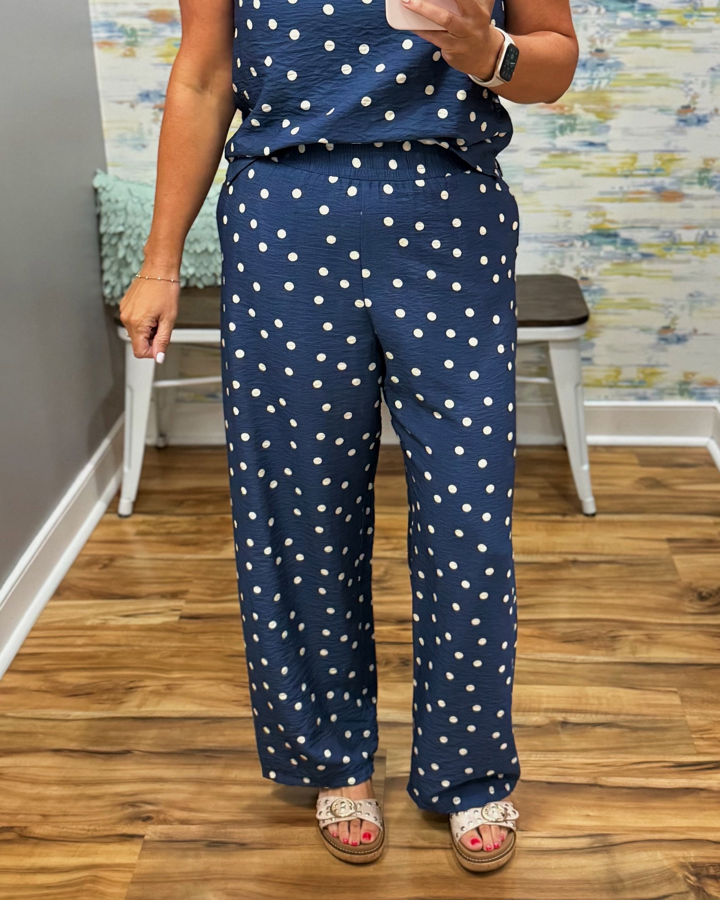 Person wearing a navy blue outfit with white polka dots in a room with wooden flooring and a colorful wall.