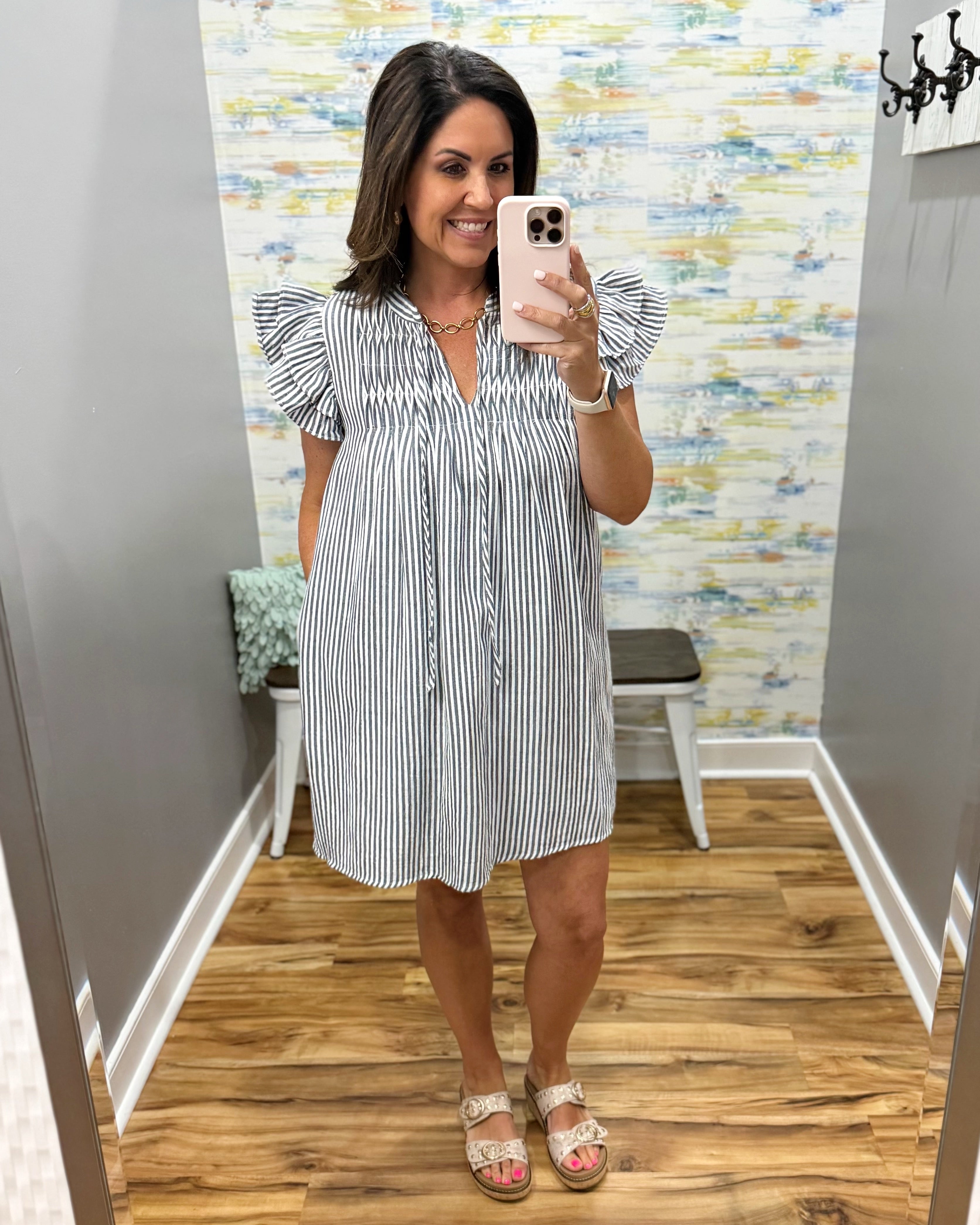 Woman taking a mirror selfie wearing a black and white striped dress in a room with a colorful wall.