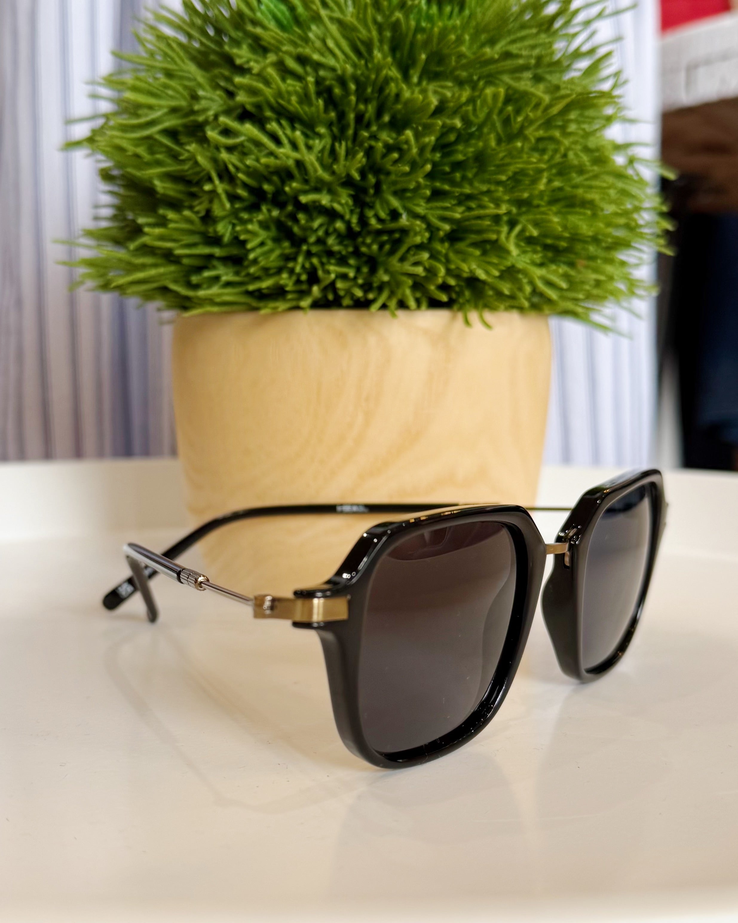 Sunglasses on a white surface with a potted plant in the background