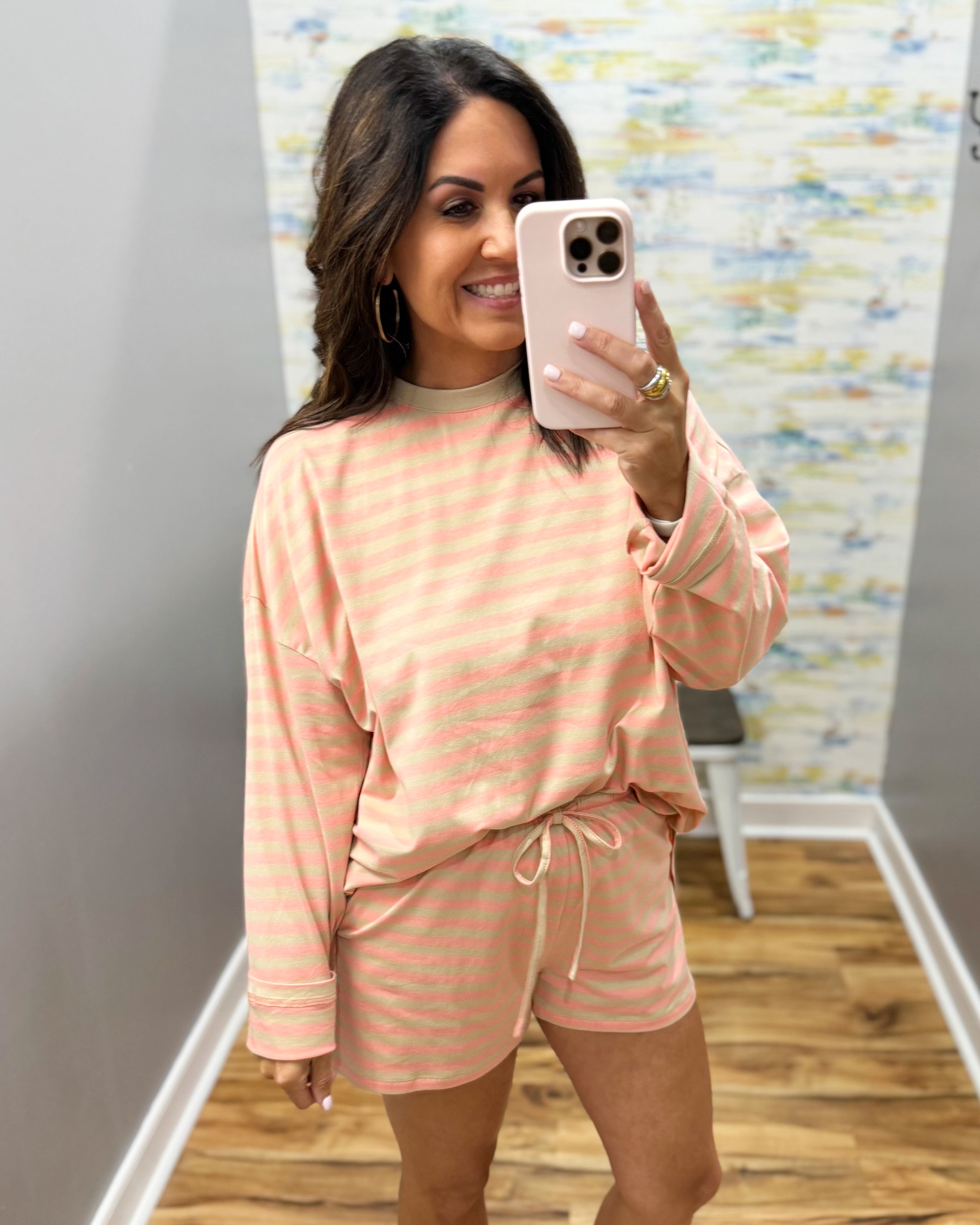 A woman takes a mirror selfie wearing a peach and white striped long-sleeve top and matching shorts set in a fitting room.
