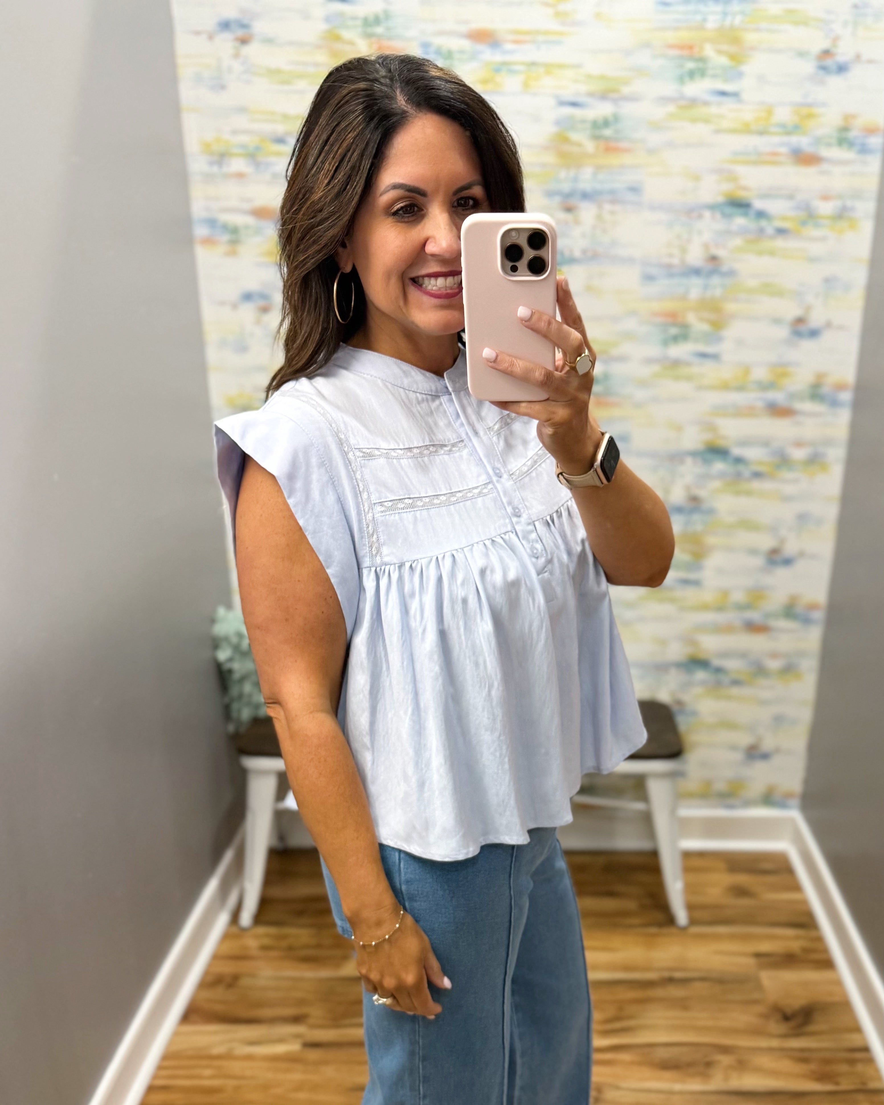 Woman taking a mirror selfie wearing a light blue top and jeans in a room with a colorful wall.