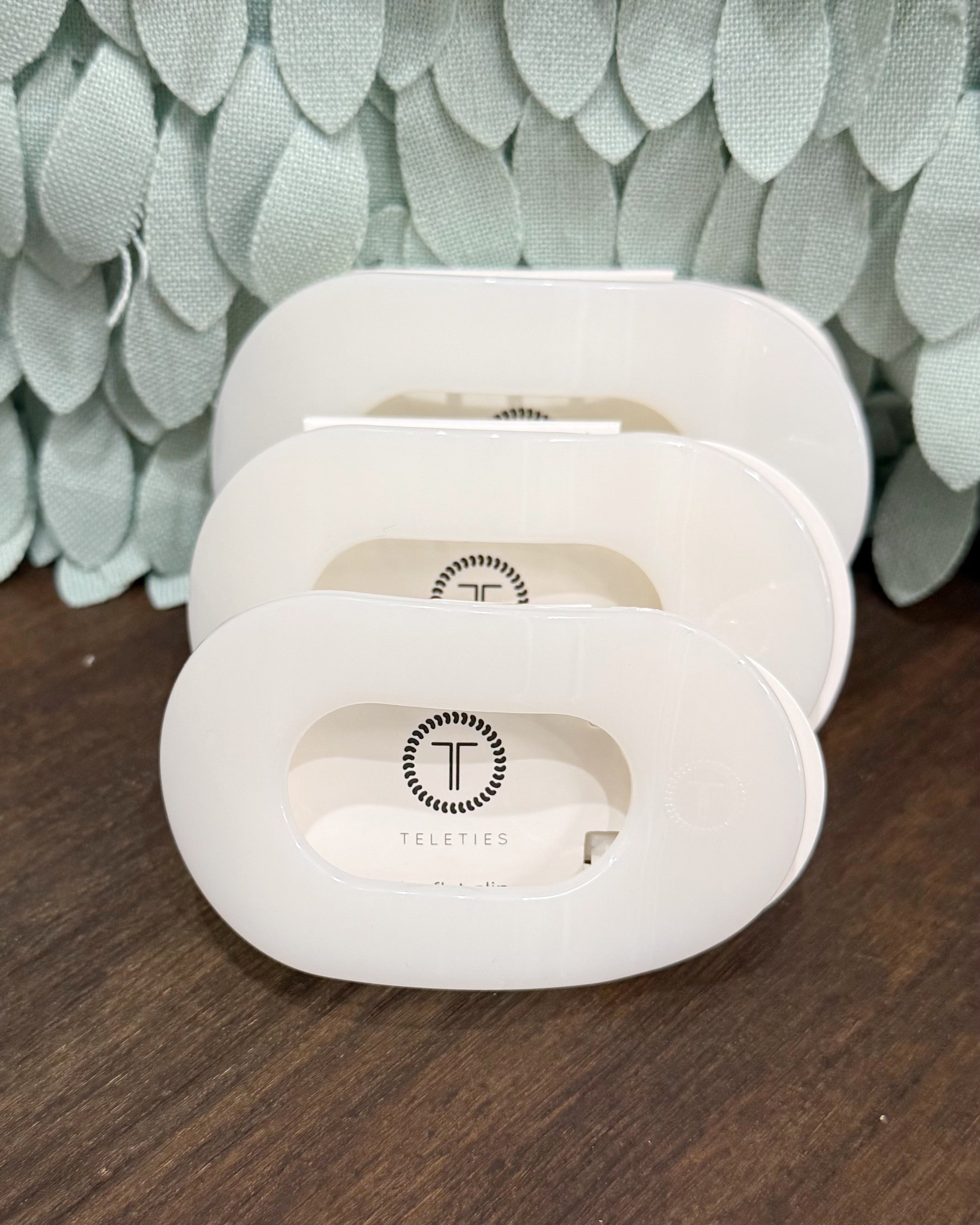 Three white electronic devices with a brand logo on a wooden surface and leafy background