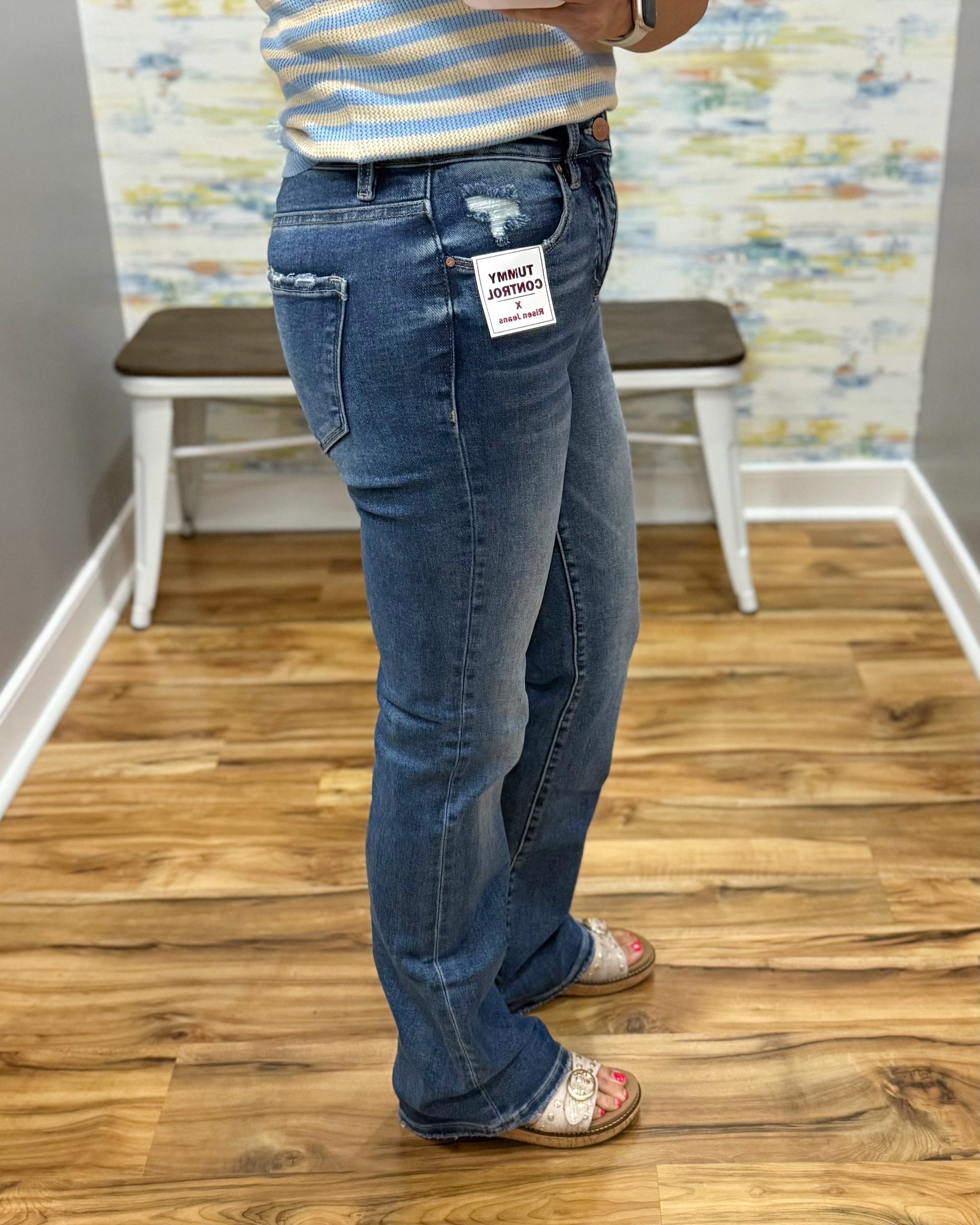 Person wearing blue jeans with a visible brand tag on a wooden floor.