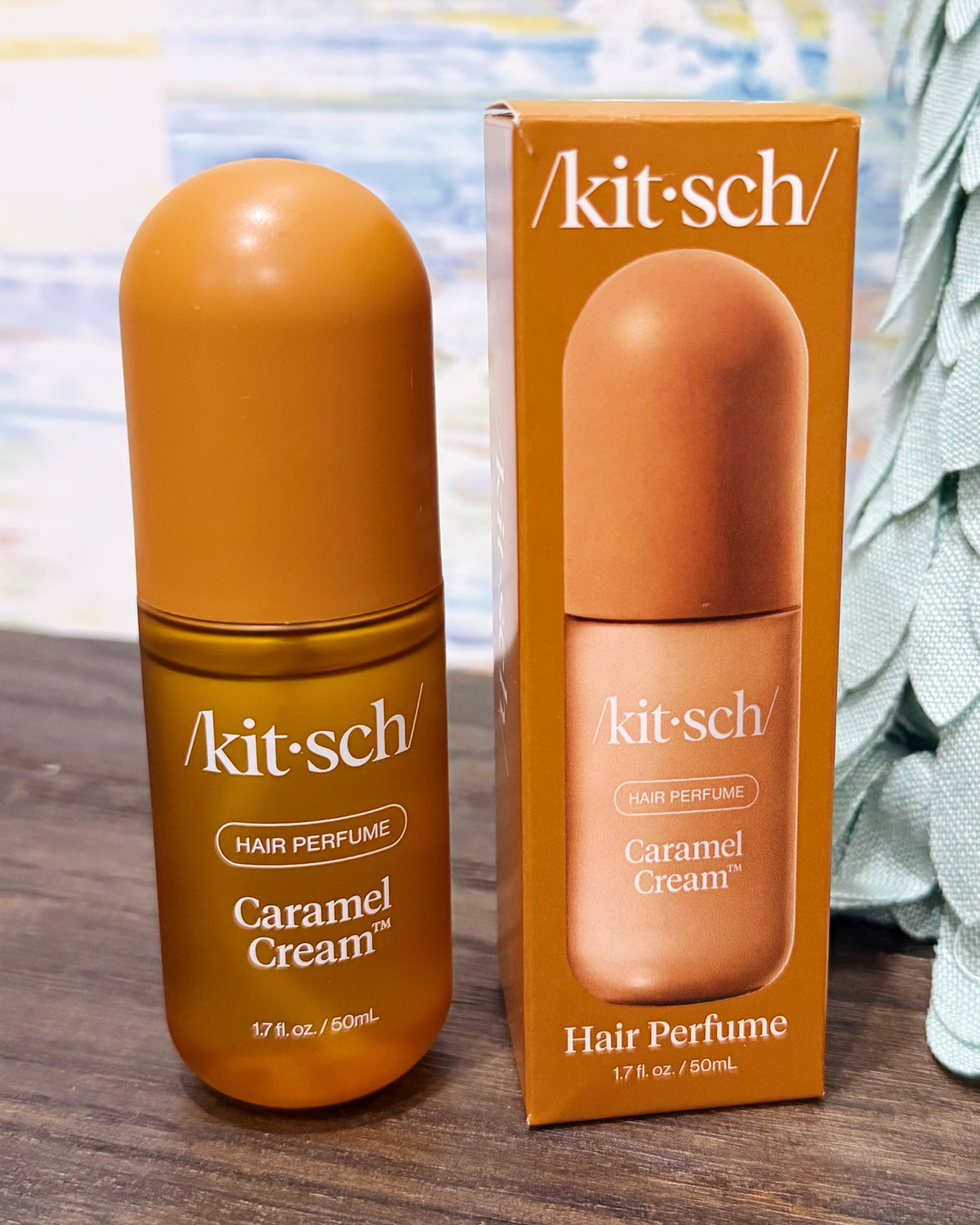 Kit Sch Caramel Cream hair perfume bottle and its matching retail box, both in a warm caramel orange-brown color, displayed on a wooden surface.