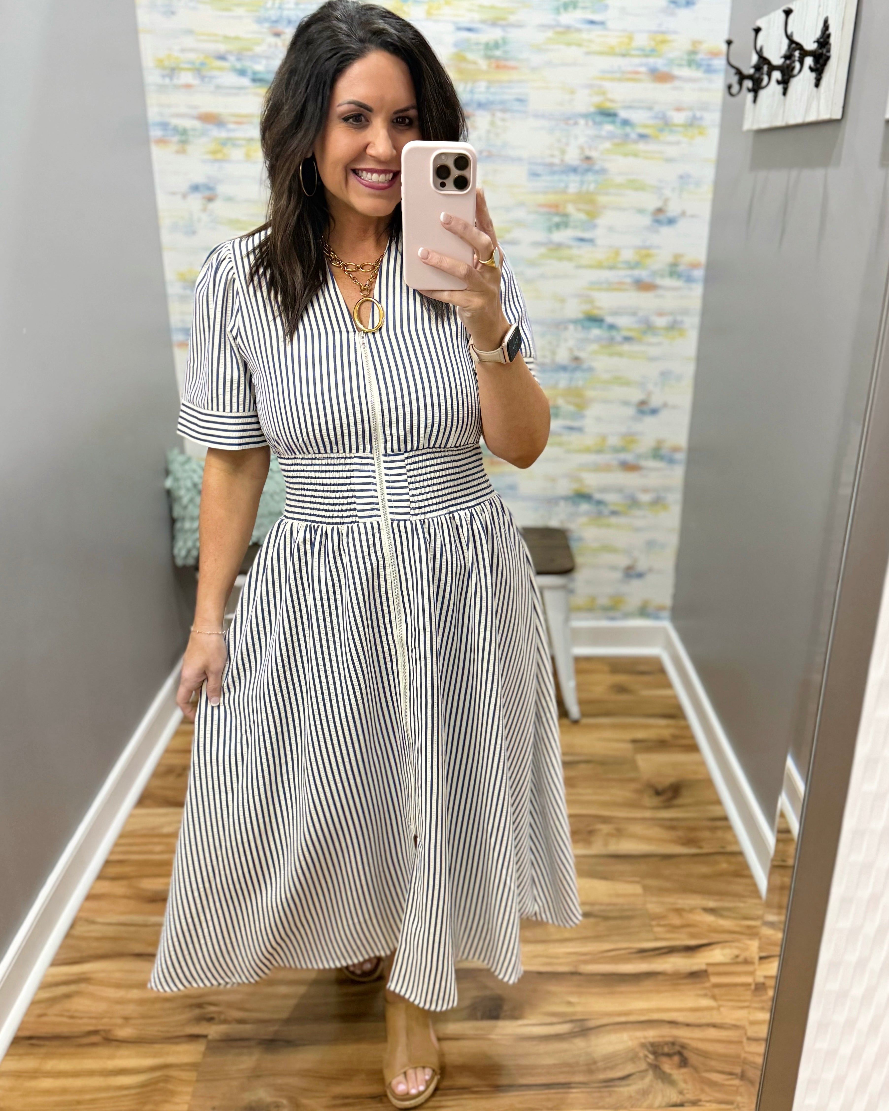 Woman wearing a black and white striped dress in a room with patterned wallpaper.