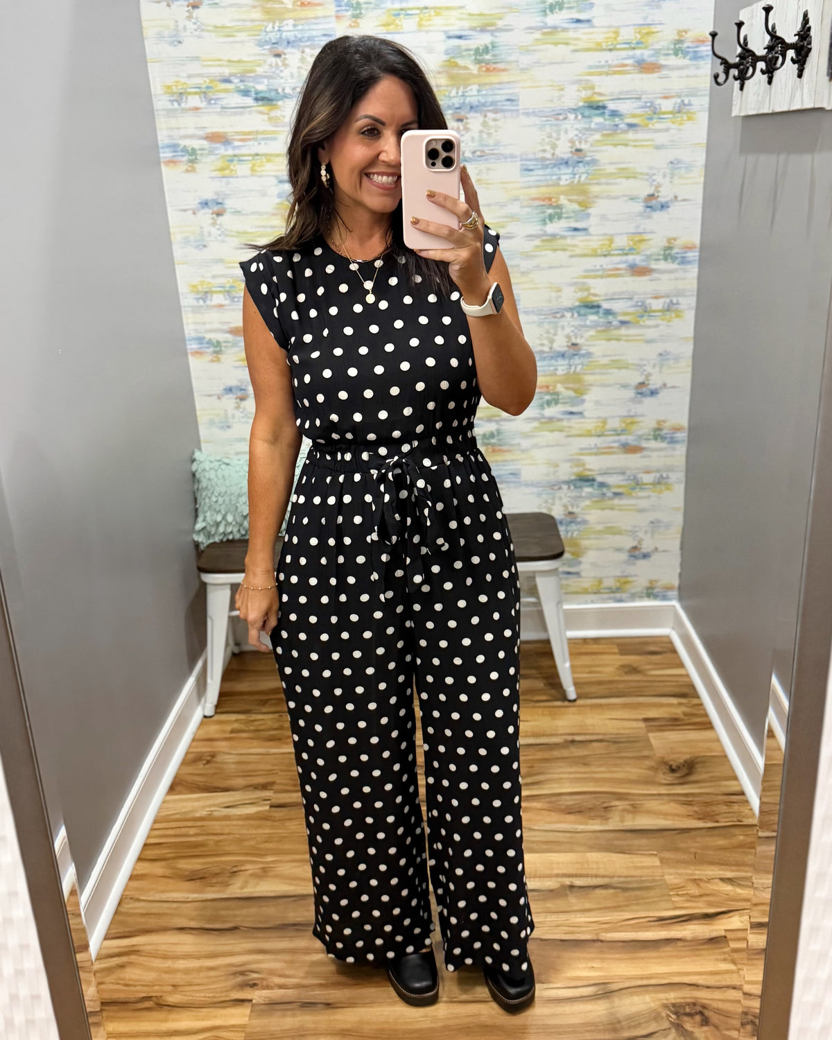 woman taking a selfie wearing a black and white polka dot jumpsuit.