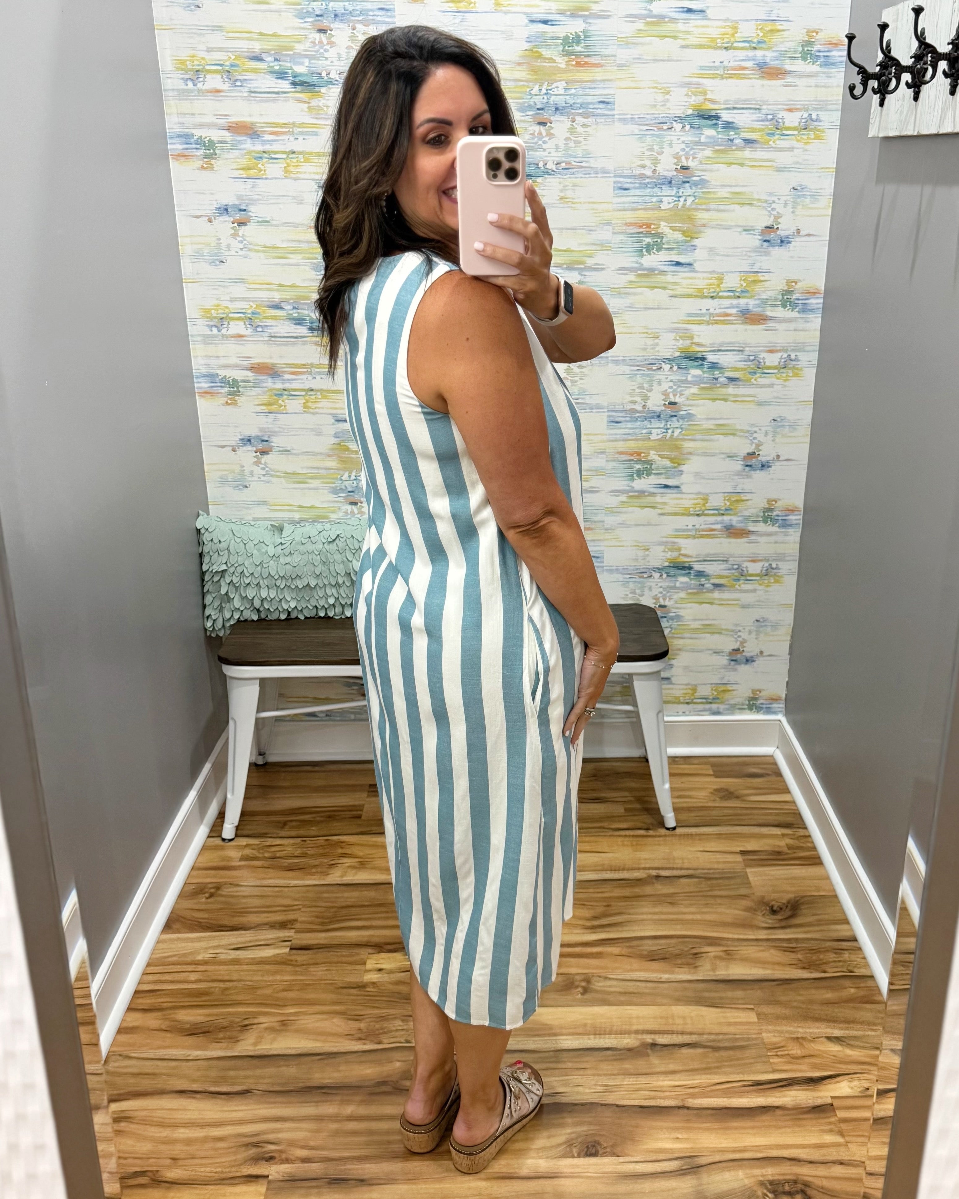 Woman taking a mirror selfie wearing a blue and white striped dress in a room with patterned wallpaper.