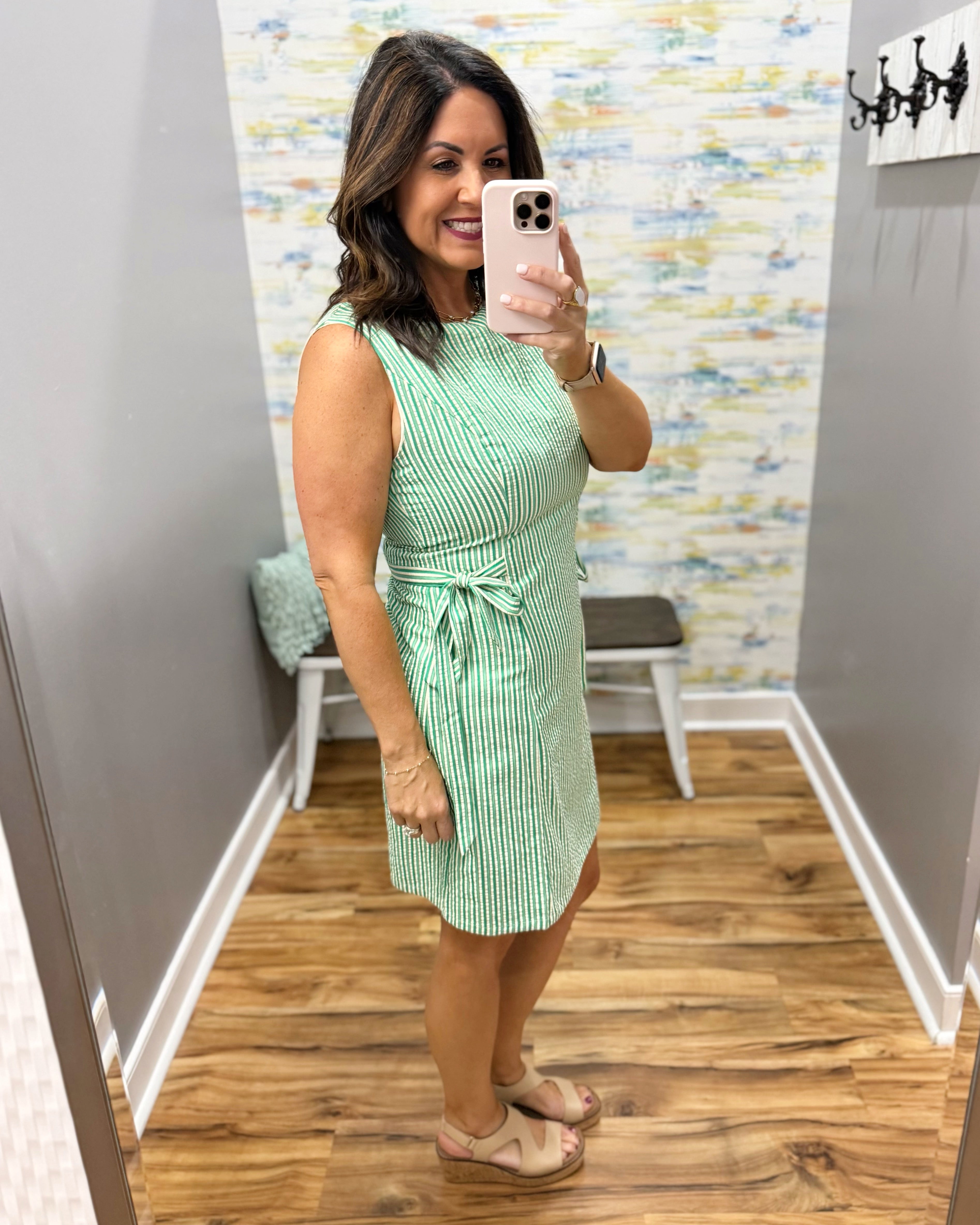 Woman taking a mirror selfie wearing a green dress in a room with a colorful wall.