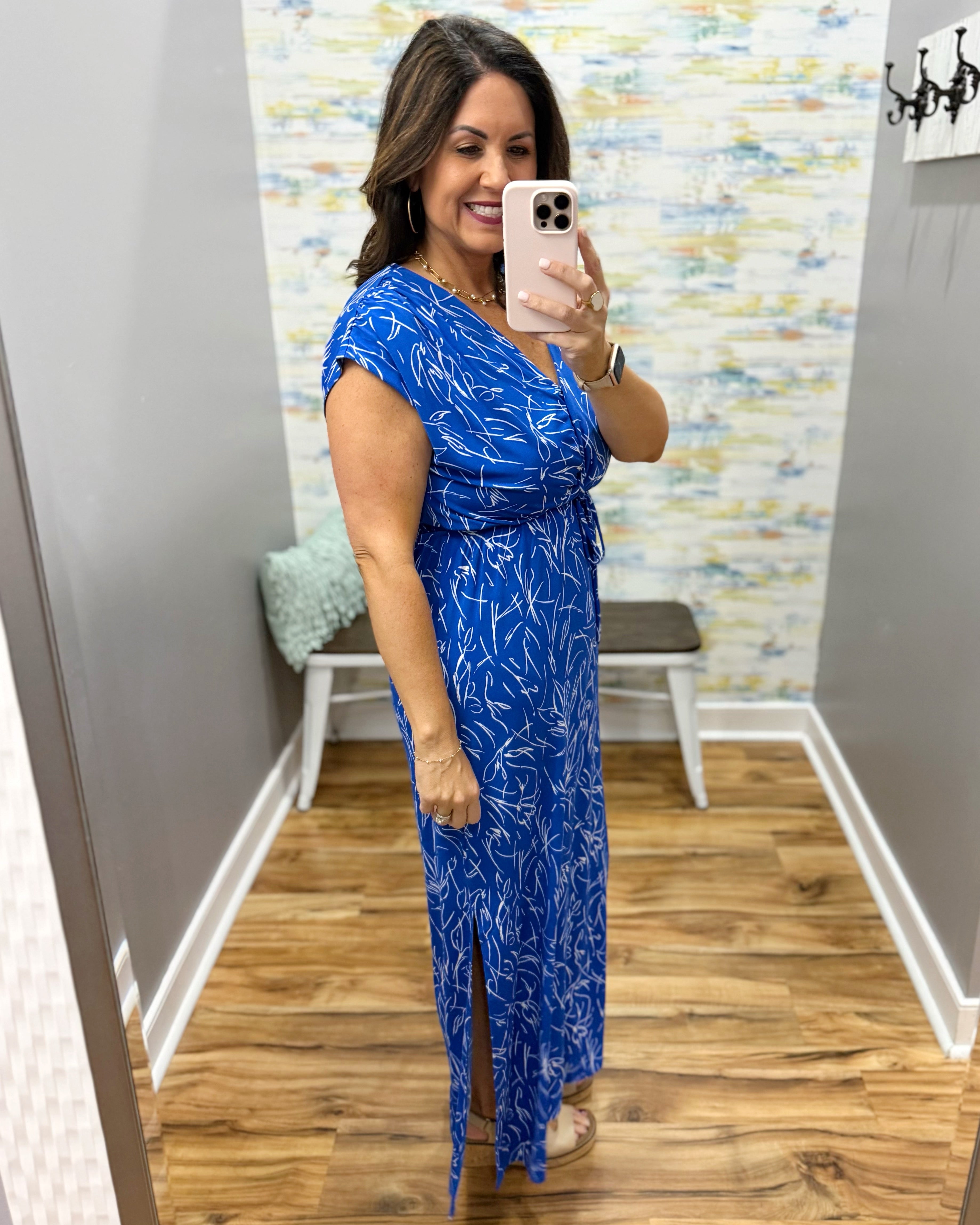 Woman taking a mirror selfie wearing a blue dress with a pattern in a room with a colorful wall.