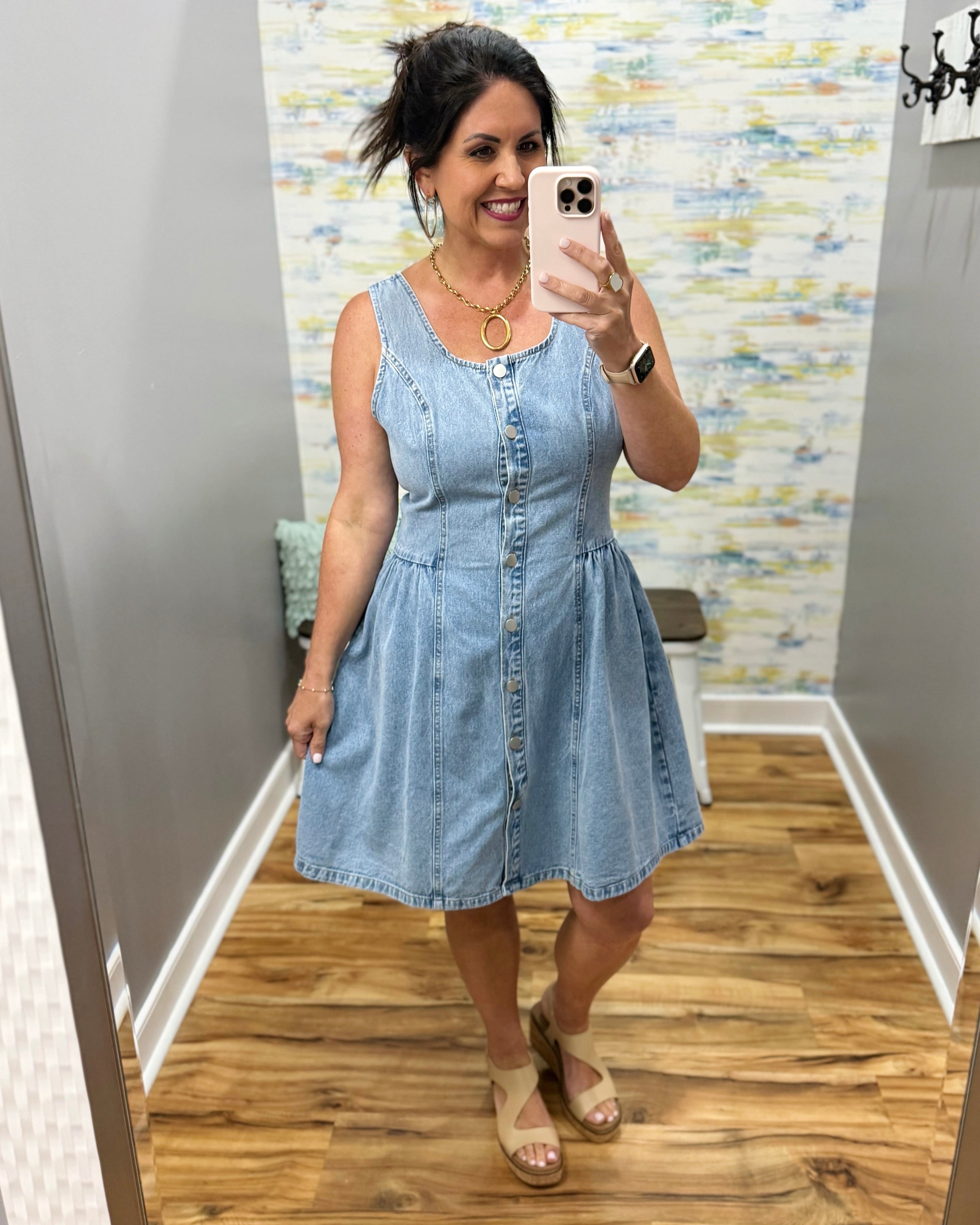 Woman wearing a light blue denim dress taking a mirror selfie.