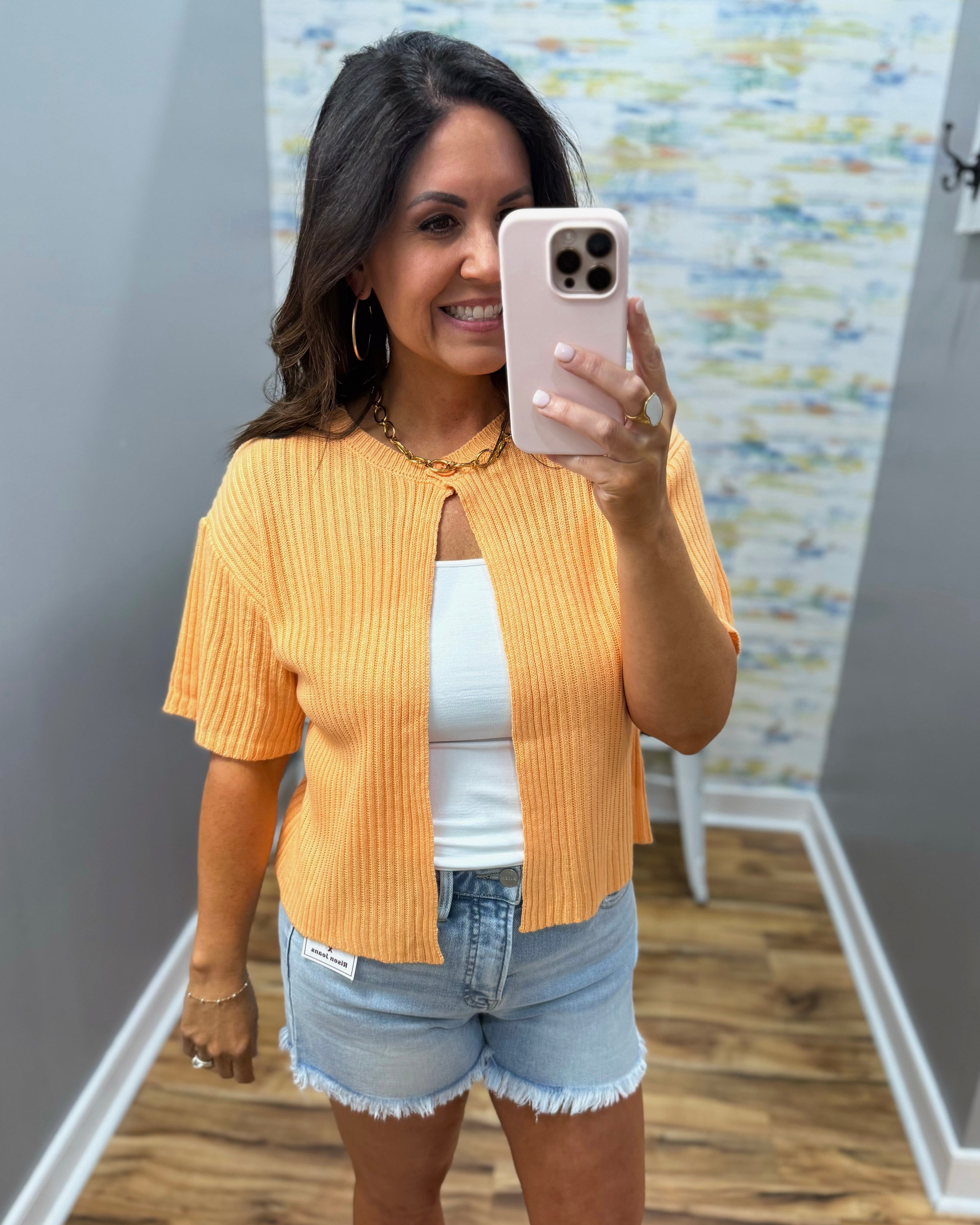 Woman taking a mirror selfie wearing a yellow ribbed top and denim shorts.