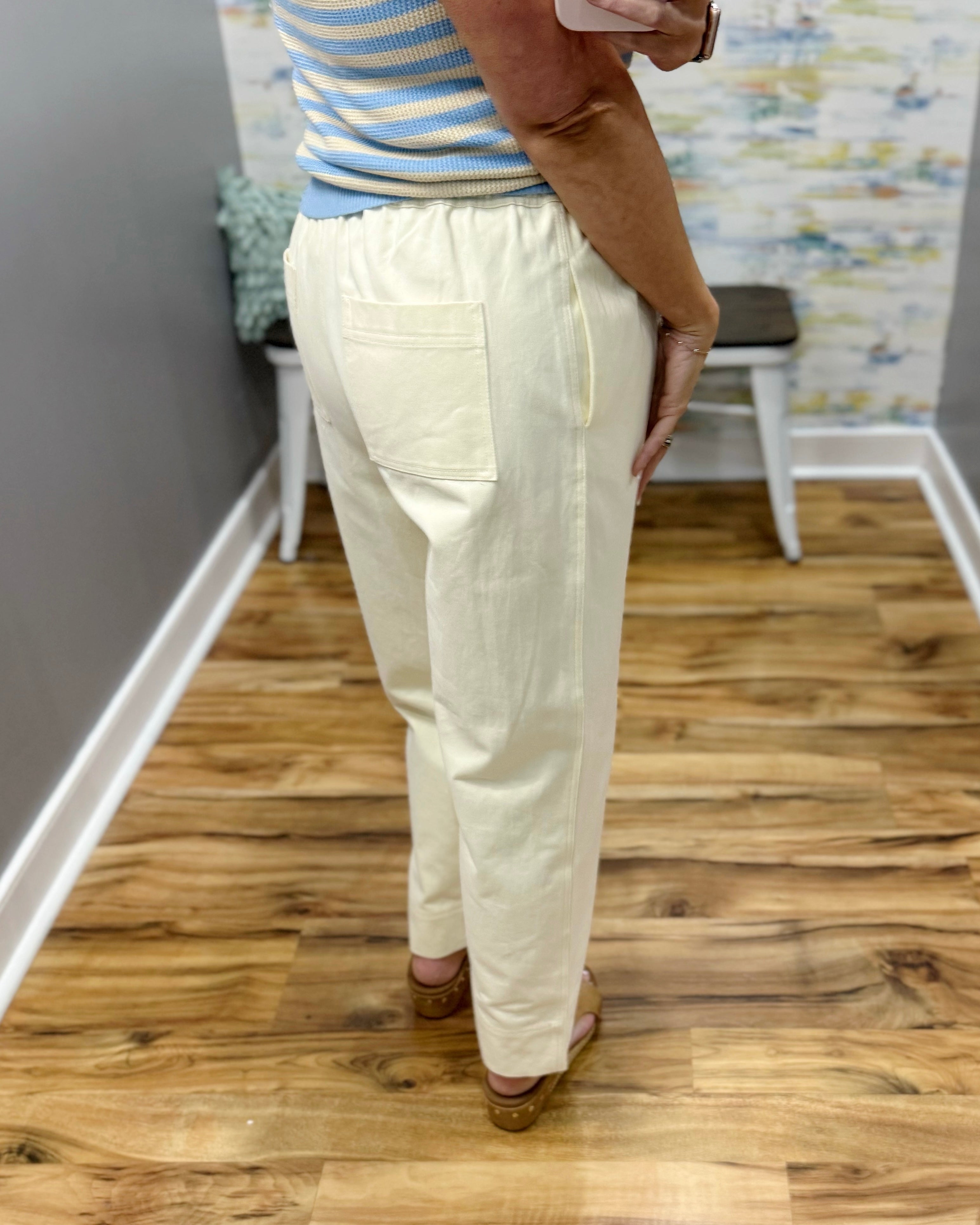 Person wearing cream-colored pants standing on a wooden floor.