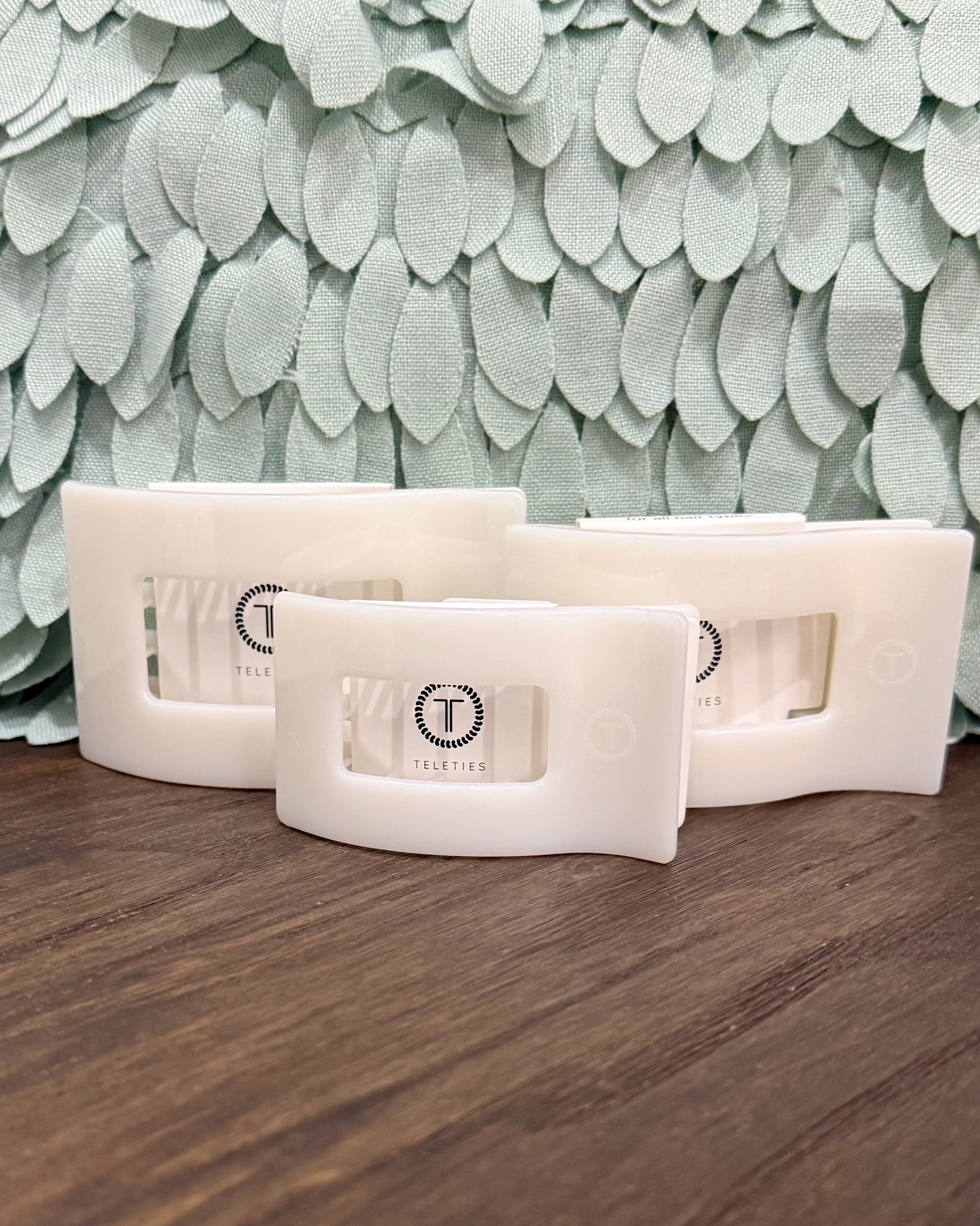White textured wall art pieces on a wooden surface with a leaf-patterned wall in the background.