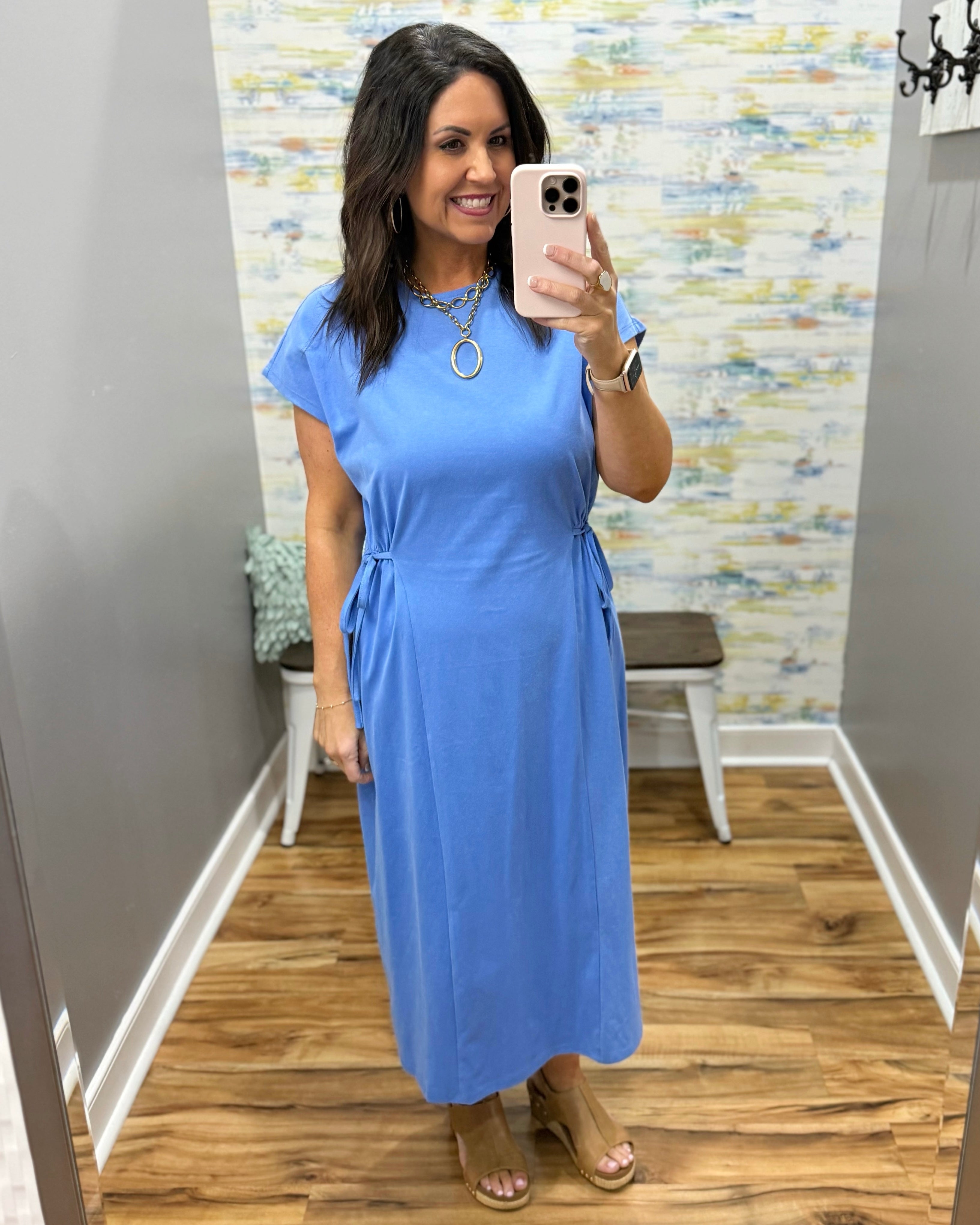 Woman wearing a blue dress in a room with a patterned wall.