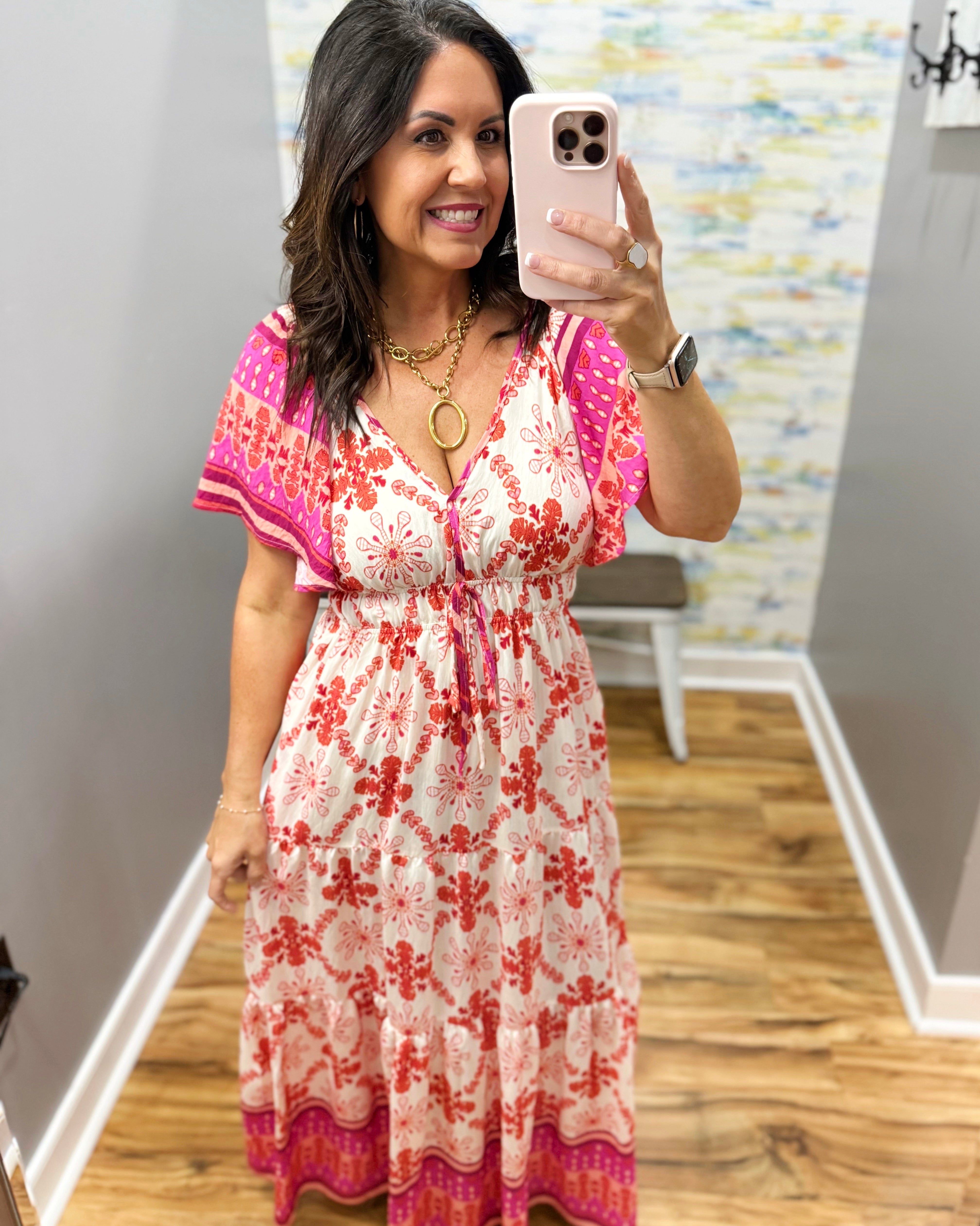 Woman taking a mirror selfie wearing a floral dress in a room with patterned wallpaper.