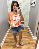 Woman taking a mirror selfie wearing a sleeveless top and denim shorts in a room with a colorful wall.