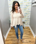 Woman taking a mirror selfie wearing a beige cardigan and blue jeans in a room with patterned wallpaper.