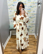 woman wearing a cream maxi dress with brown, black and taupe floral pattern. 