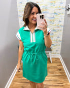 Woman taking a mirror selfie wearing a green dress with white and red accents.