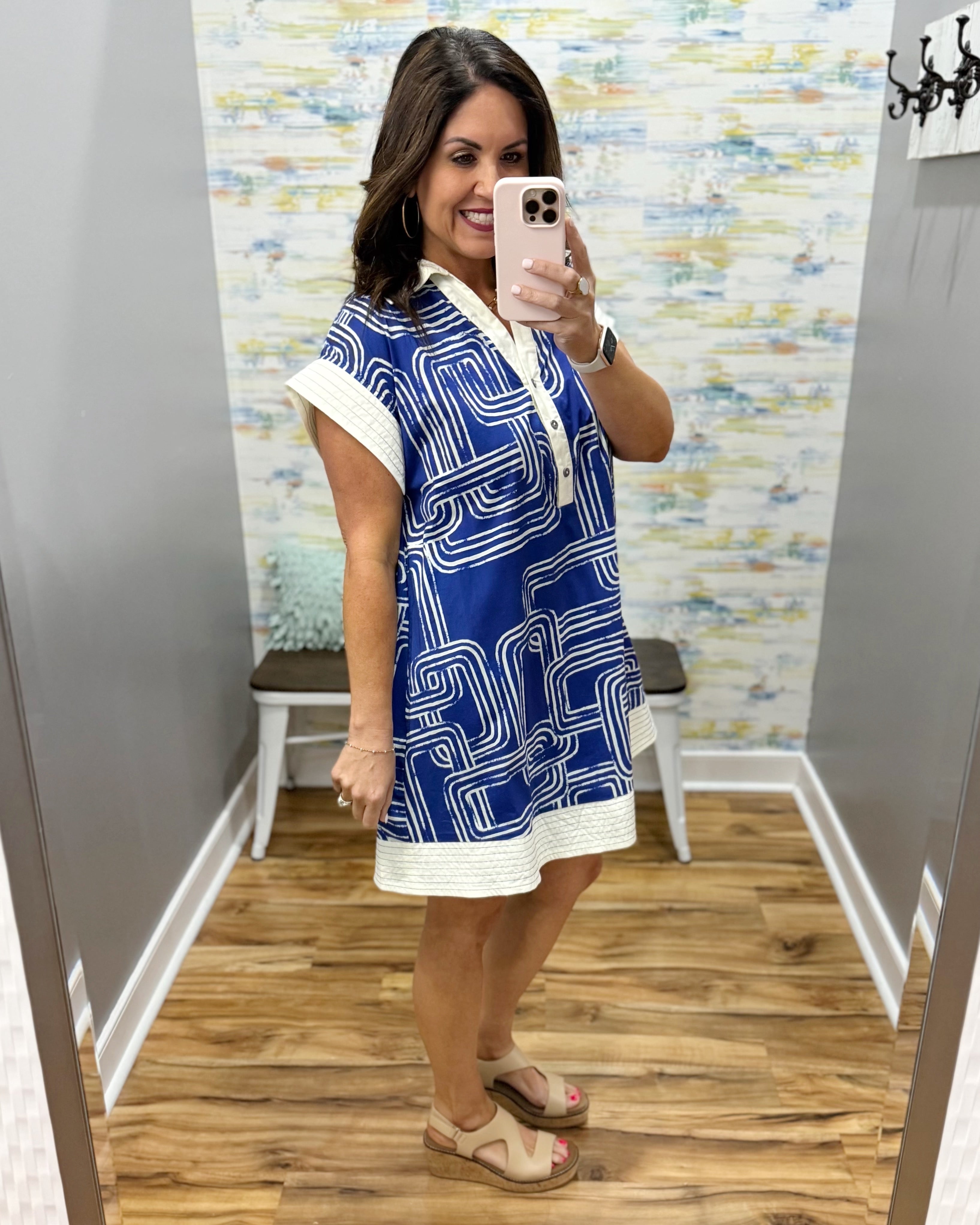Woman taking a mirror selfie wearing a blue and white dress with a geometric pattern.