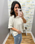 Woman taking a mirror selfie wearing a natural sweater and jeans in a room with a textured wall.