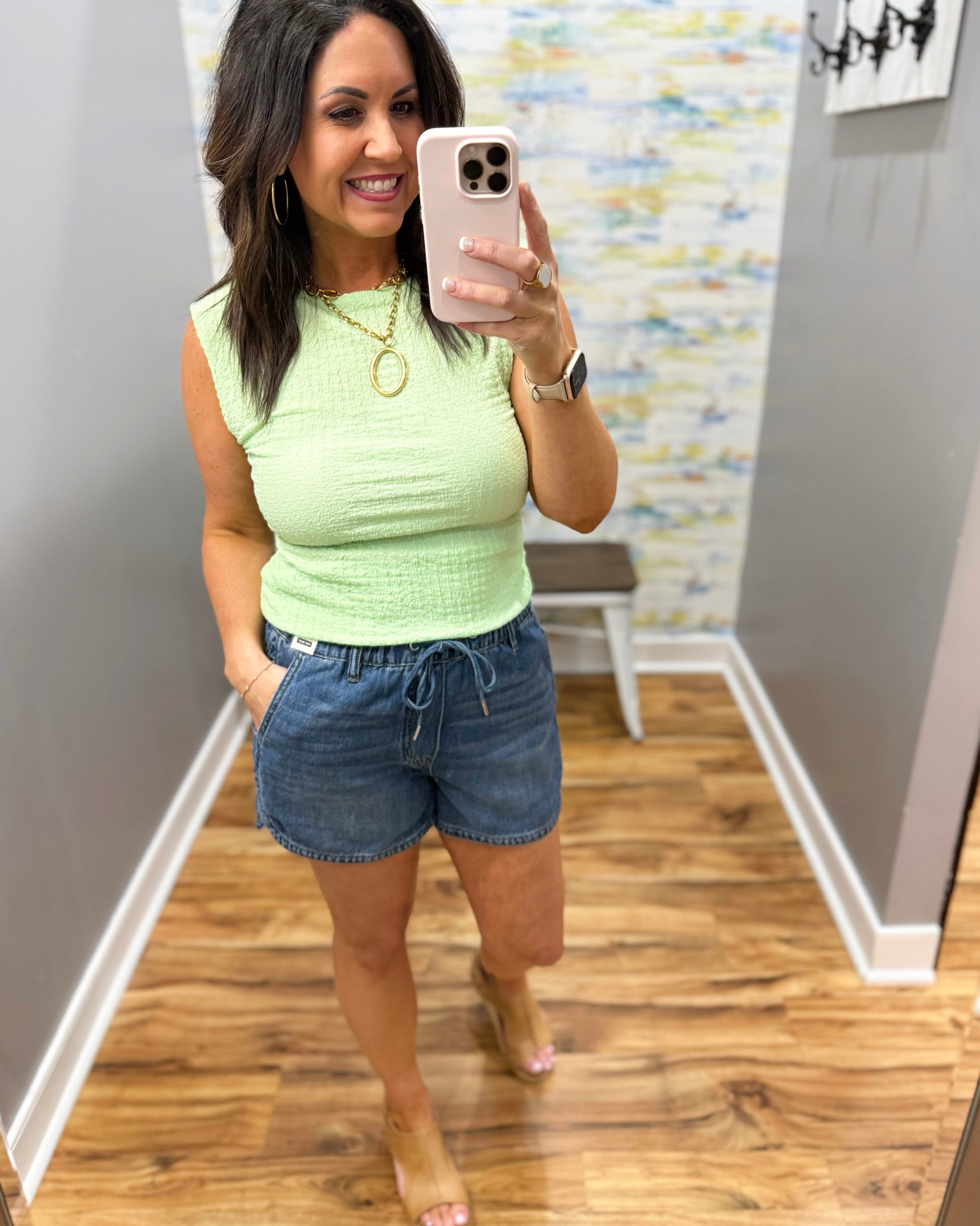 Woman wearing a light green top and denim shorts in a room with wooden flooring.