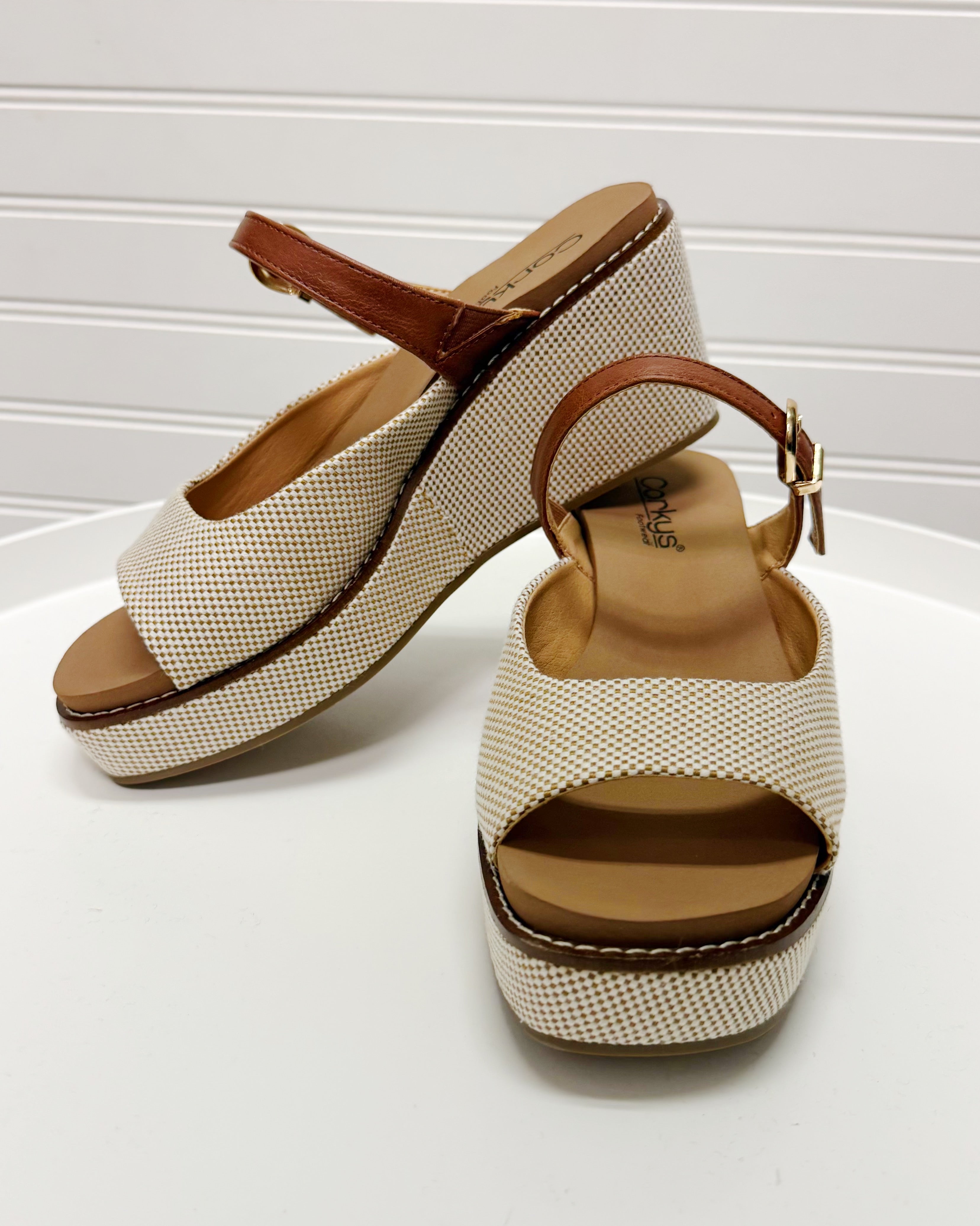 Pair of beige wedge sandals with brown straps on a white background