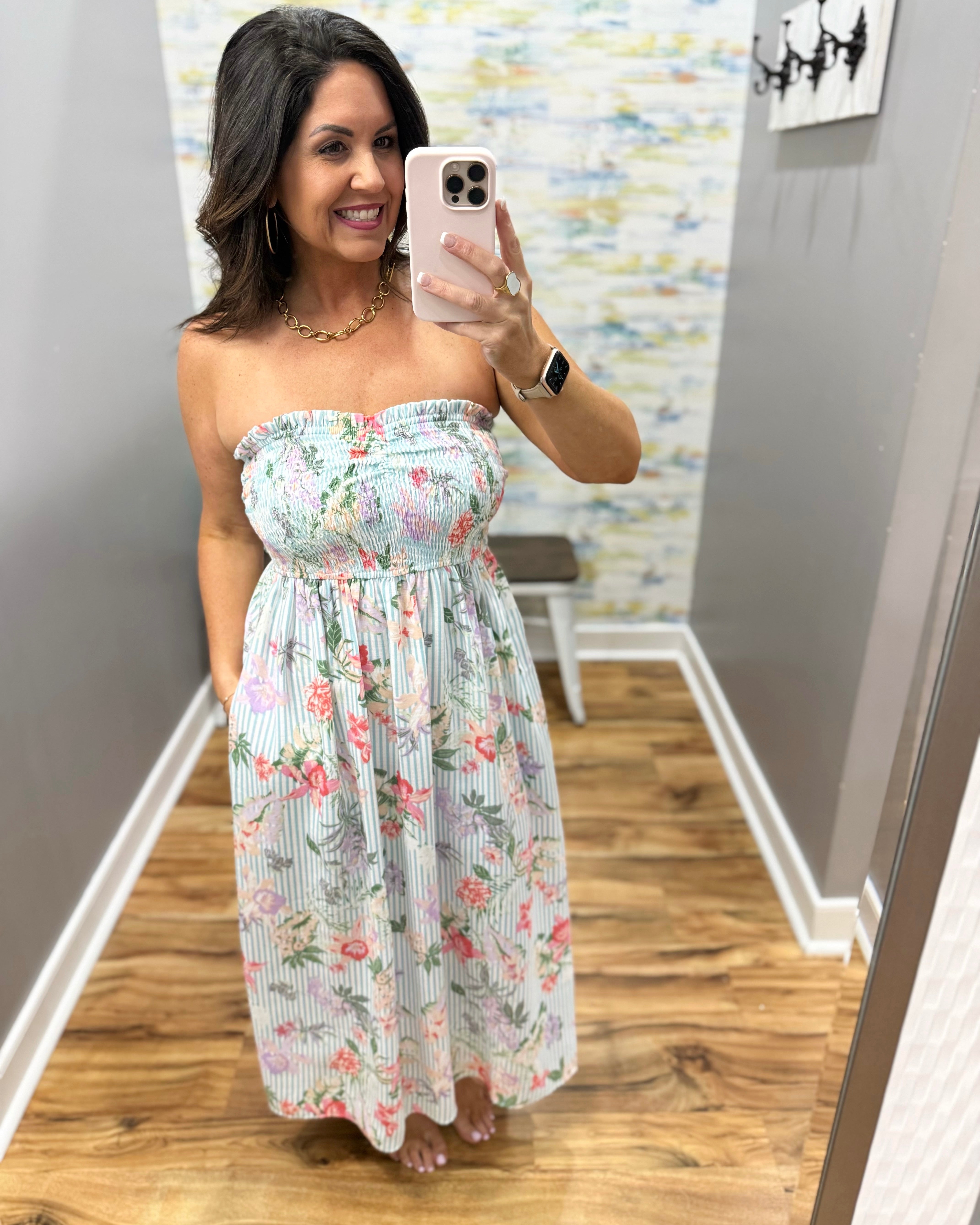 Woman taking a mirror selfie wearing a floral strapless dress in a room with a colorful wall.