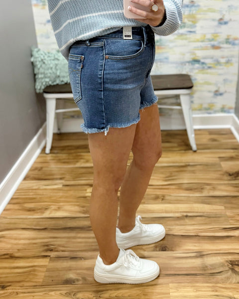 Person wearing a light blue denim shorts and white sneakers on a wooden floor.