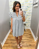 Woman taking a mirror selfie wearing a striped dress in a room with colorful wallpaper.