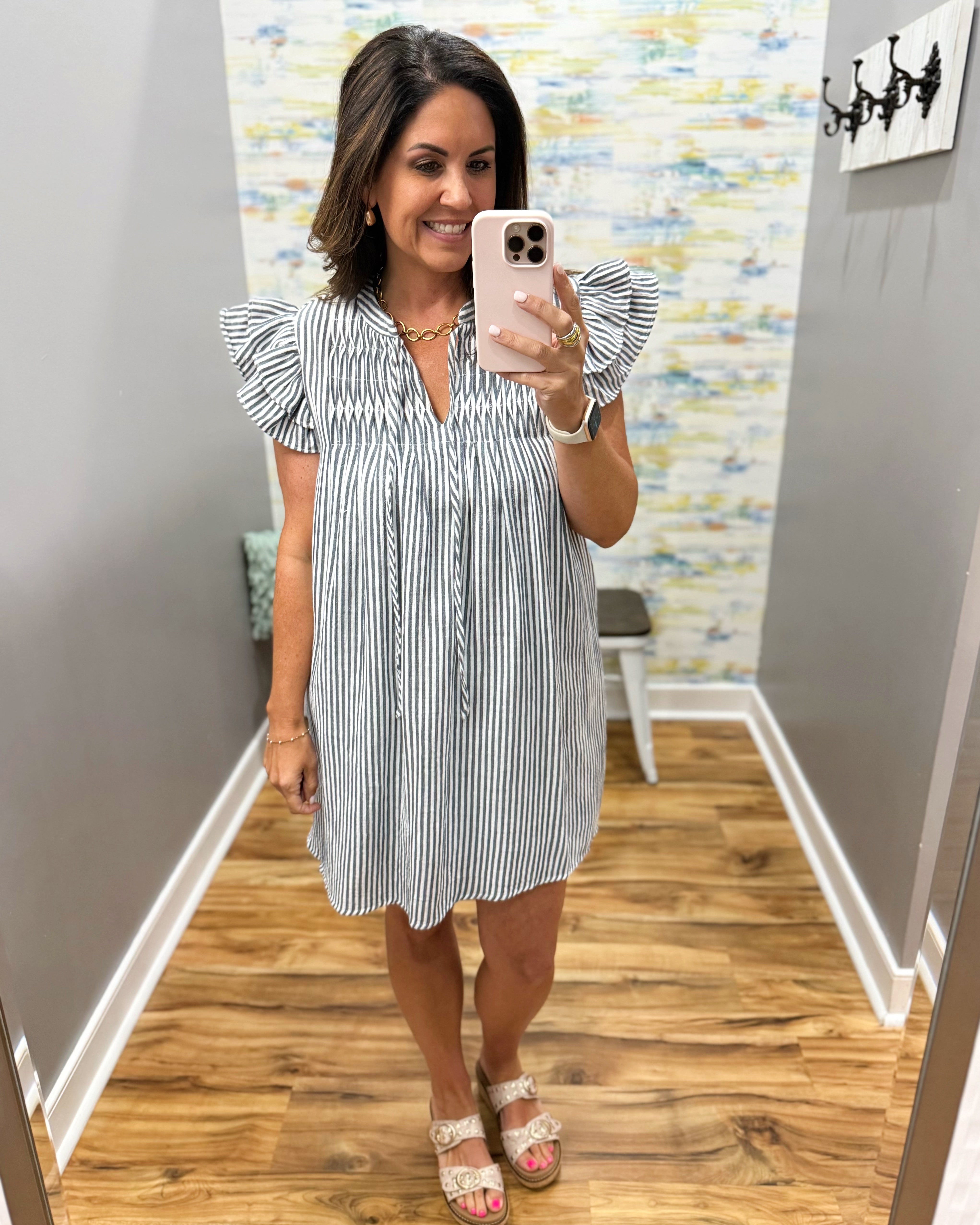 Woman taking a mirror selfie wearing a striped dress in a room with colorful wallpaper.