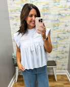 Woman taking a mirror selfie wearing a white blouse and blue jeans in a room with colorful wall art.