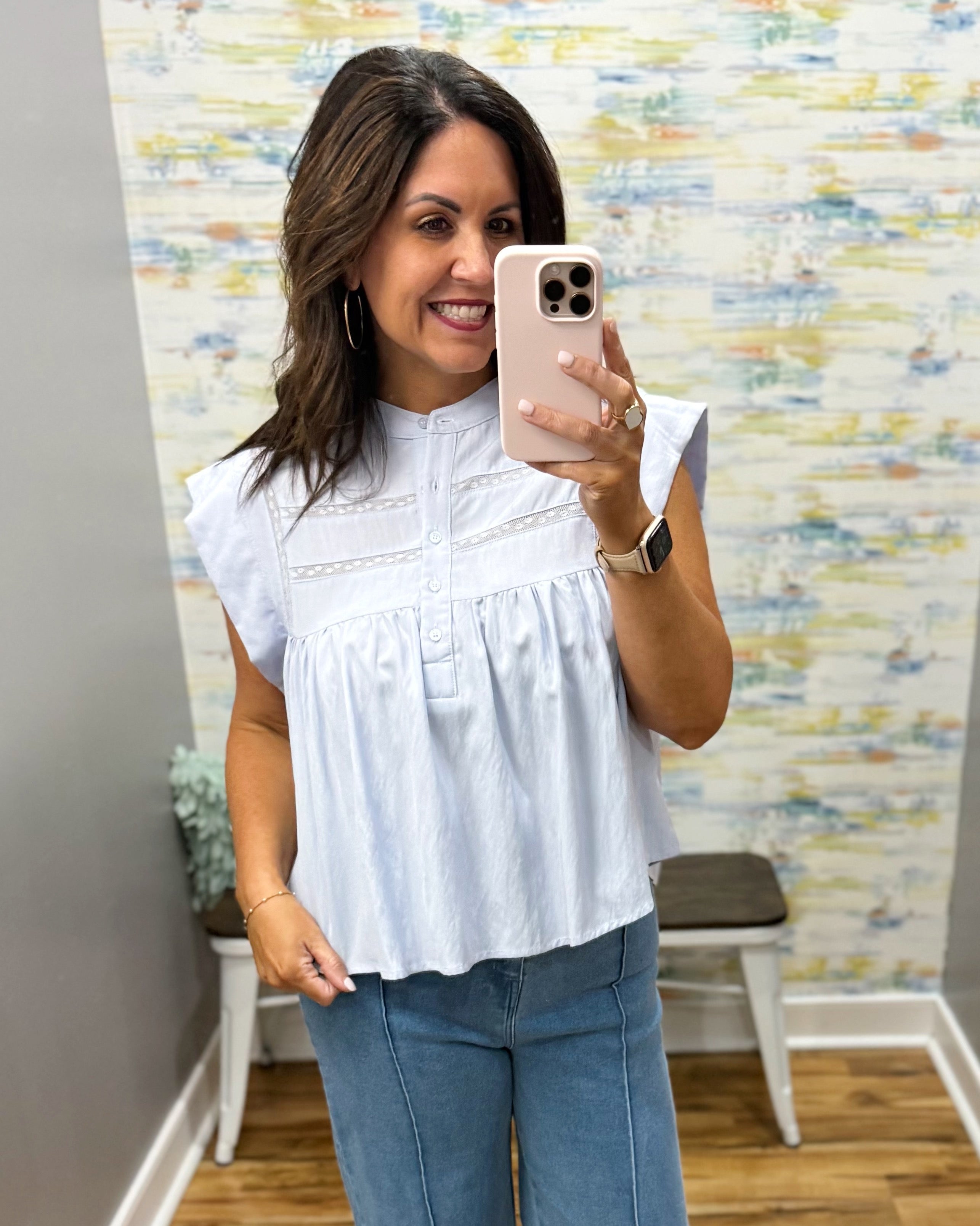 Woman taking a mirror selfie wearing a white blouse and blue jeans in a room with colorful wall art.