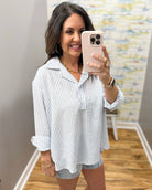 Woman taking a mirror selfie wearing a striped shirt and shorts, holding a phone.