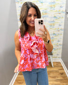 Woman taking a mirror selfie wearing a red floral top and blue jeans.