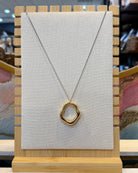 This two tone open ring pendant necklace features a sculpted organic wavy ring in polished gold tone hanging from a silver tone curb chain with a lobster clasp.