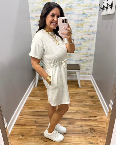 Woman wearing a neutral dress and white sneakers.