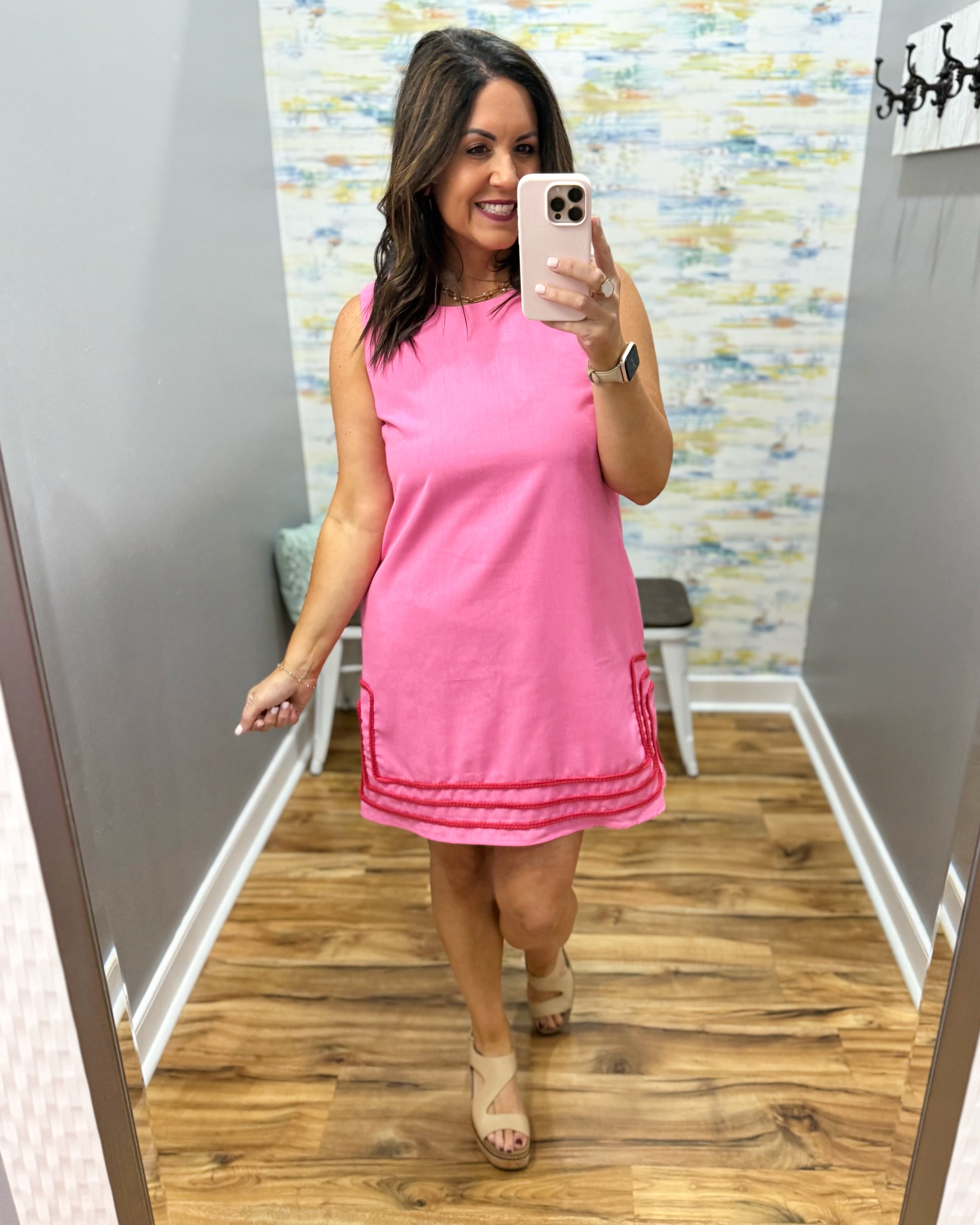 Woman taking a mirror selfie wearing a pink dress in a store.