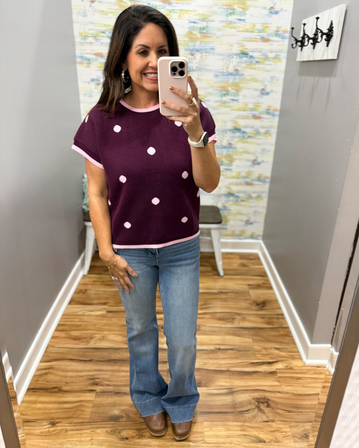 A woman takes a mirror selfie wearing a short-sleeve ringer knit top in plum with light pink trim and white polka dots, paired with light-wash blue jeans and brown shoes.