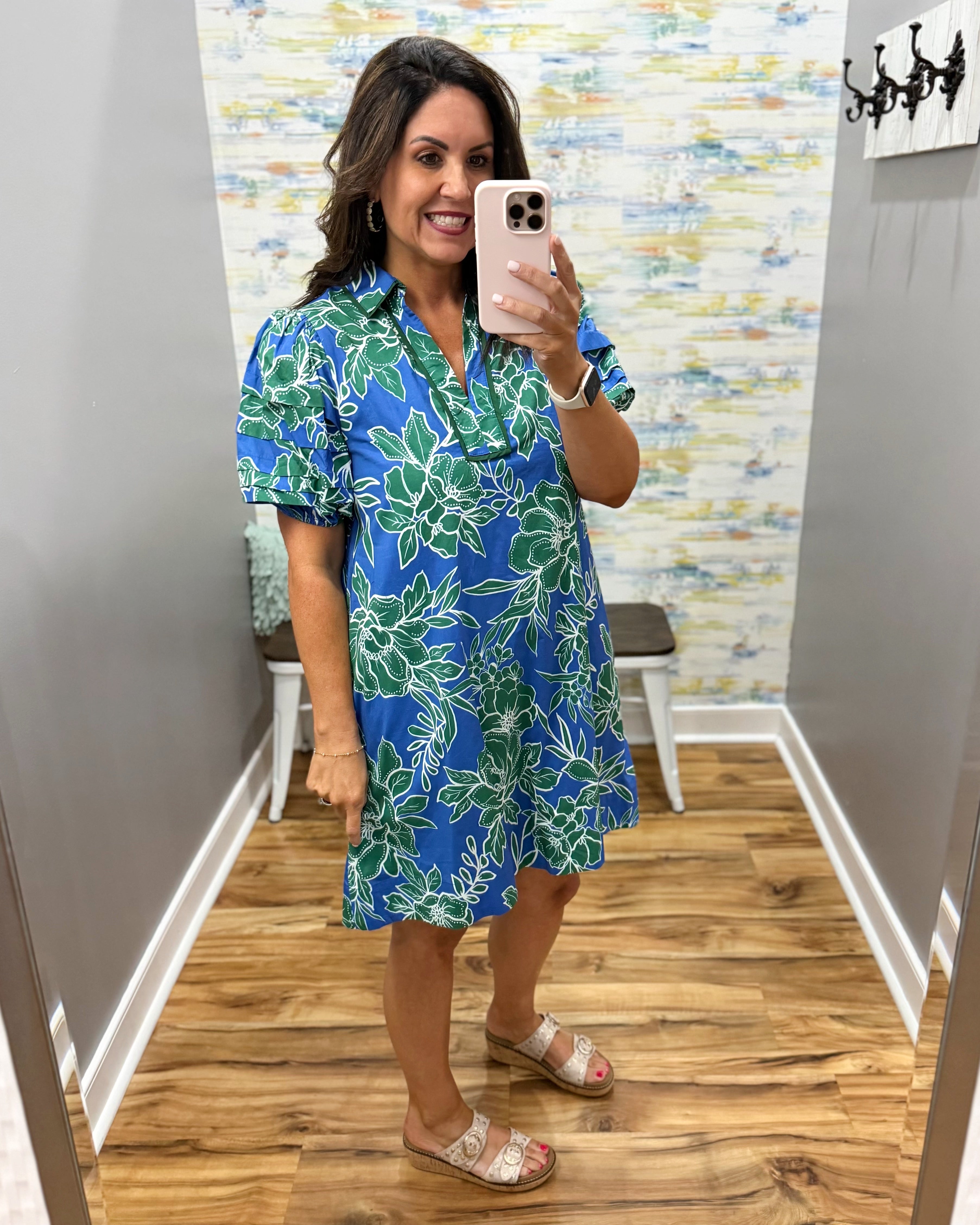 Woman wearing a blue floral dress in a room with a patterned wall.