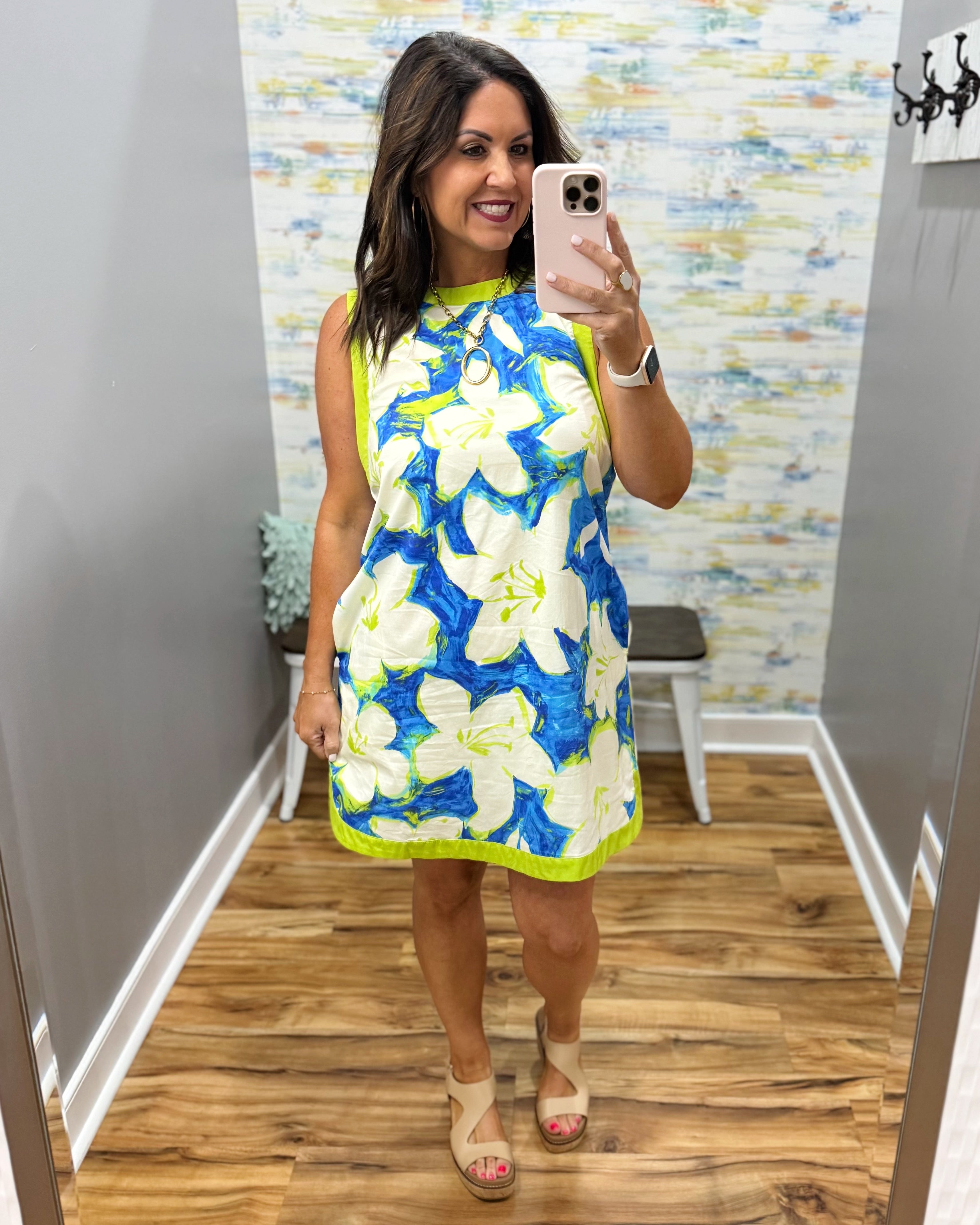 Woman taking a mirror selfie wearing a floral dress in a room with a textured wall.