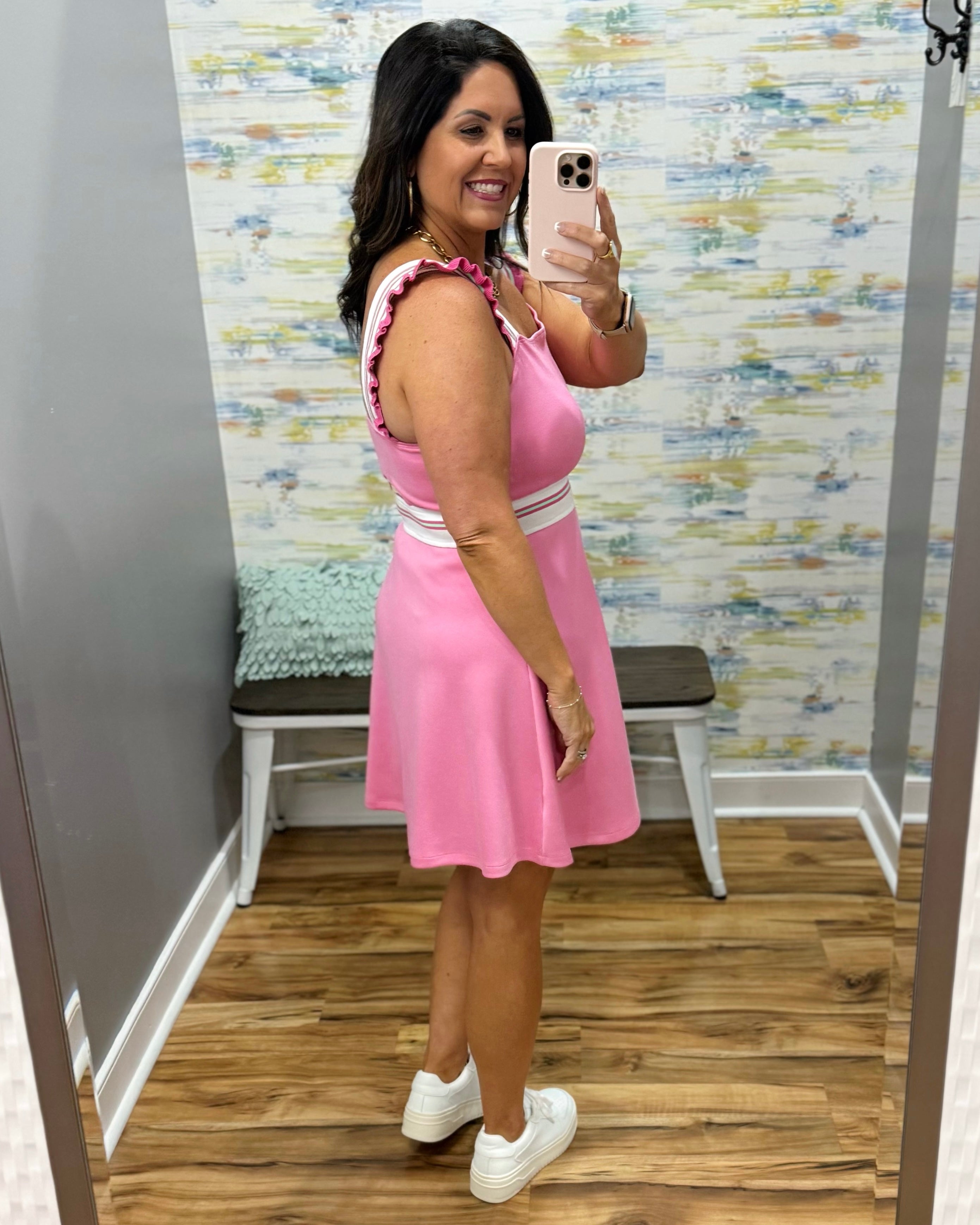 Woman taking a mirror selfie wearing a pink dress in a room with a patterned wall.