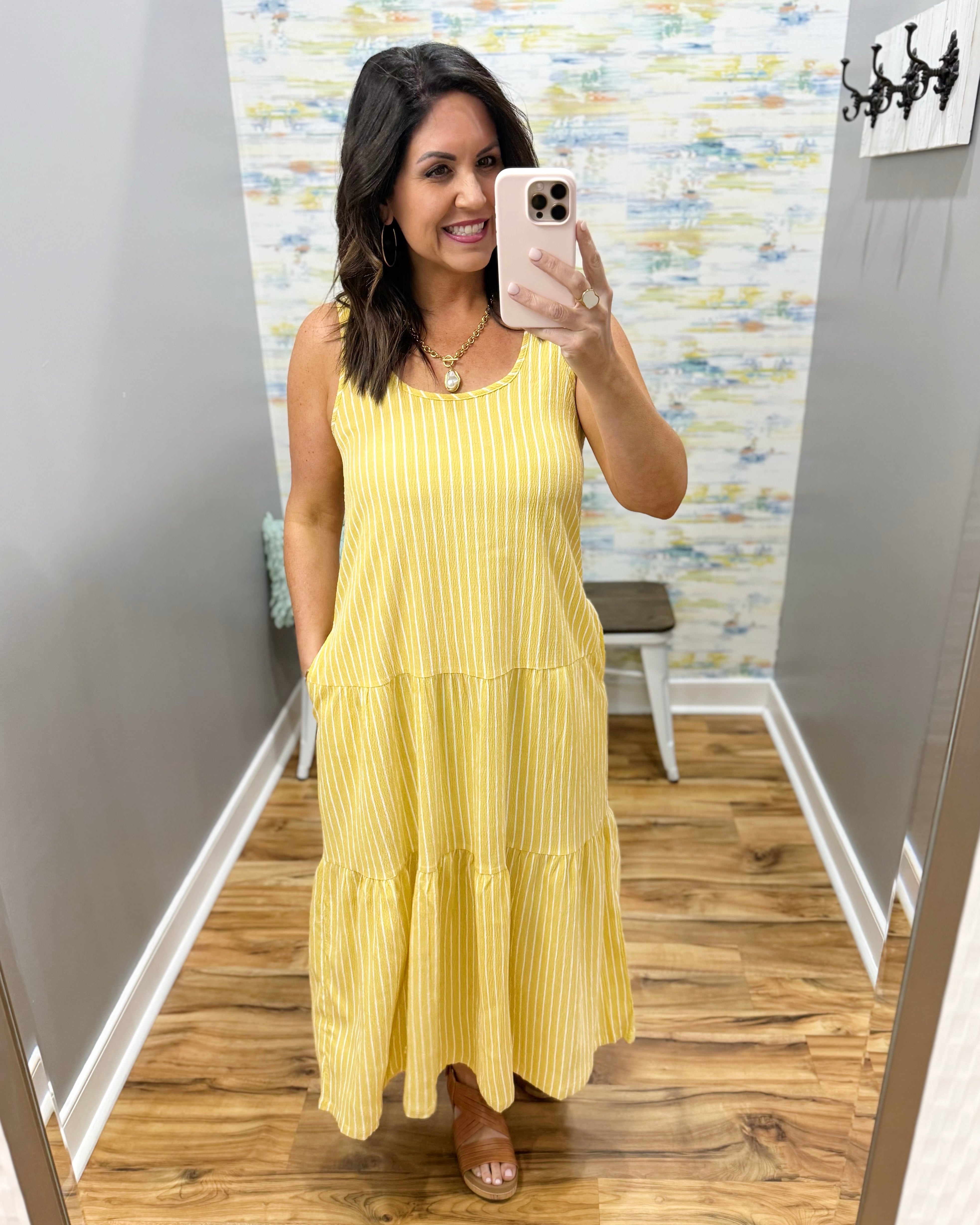 Woman wearing a yellow dress taking a mirror selfie in a room with a textured wall.