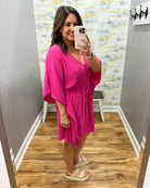 Woman taking a mirror selfie wearing a pink dress in a room with a colorful wall.