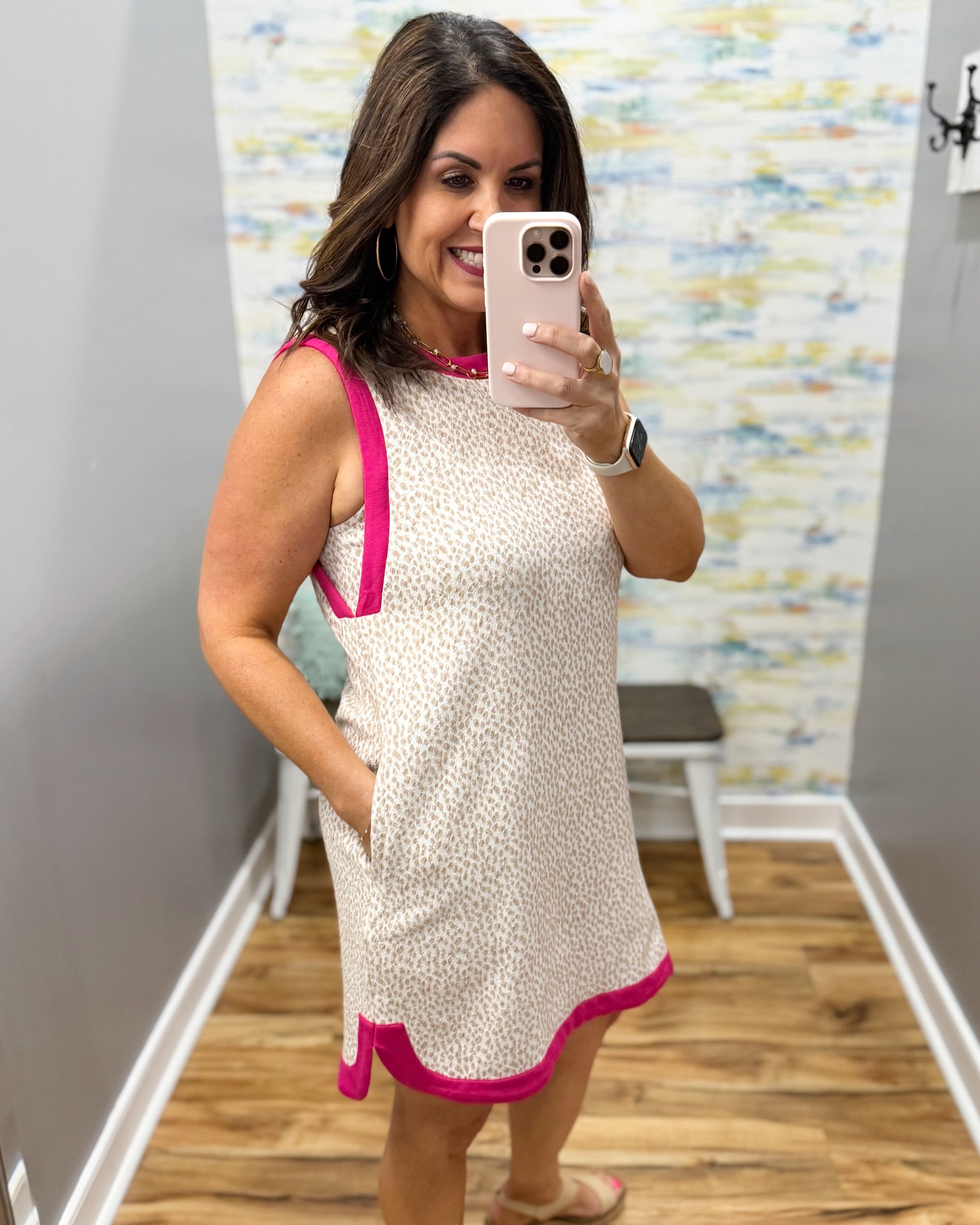 Woman taking a mirror selfie wearing a dress with pink accents in a room.