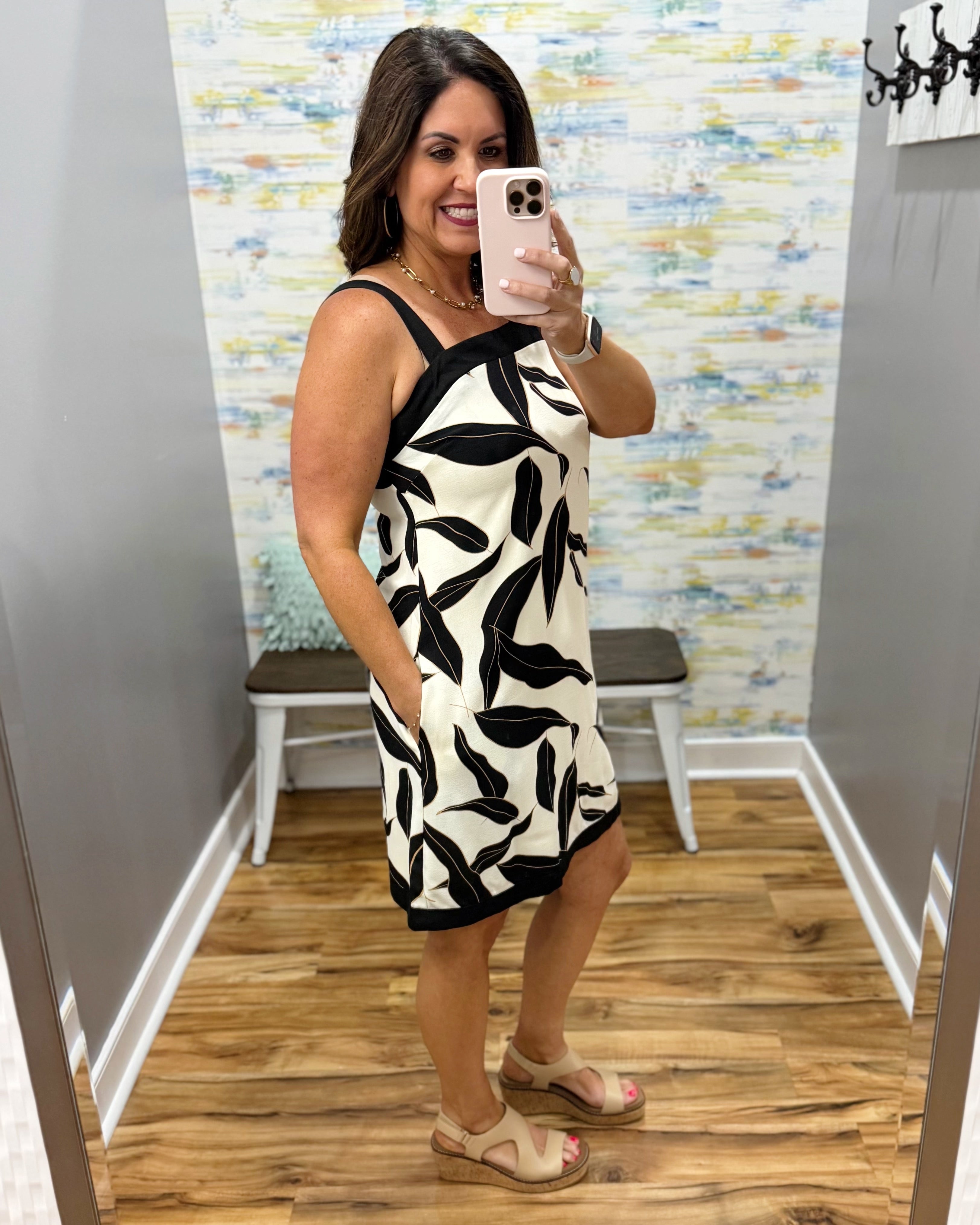 Woman taking a mirror selfie wearing a black and white patterned dress in a fitting room.