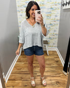 Woman taking a mirror selfie wearing a light gray sweater and denim shorts in a room with a patterned wall.